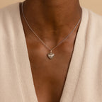 A person wearing the Vintage Heart Charm in Sterling Silver pendant necklace with a cream V-neck top—an elegant addition to any jewelry collection.