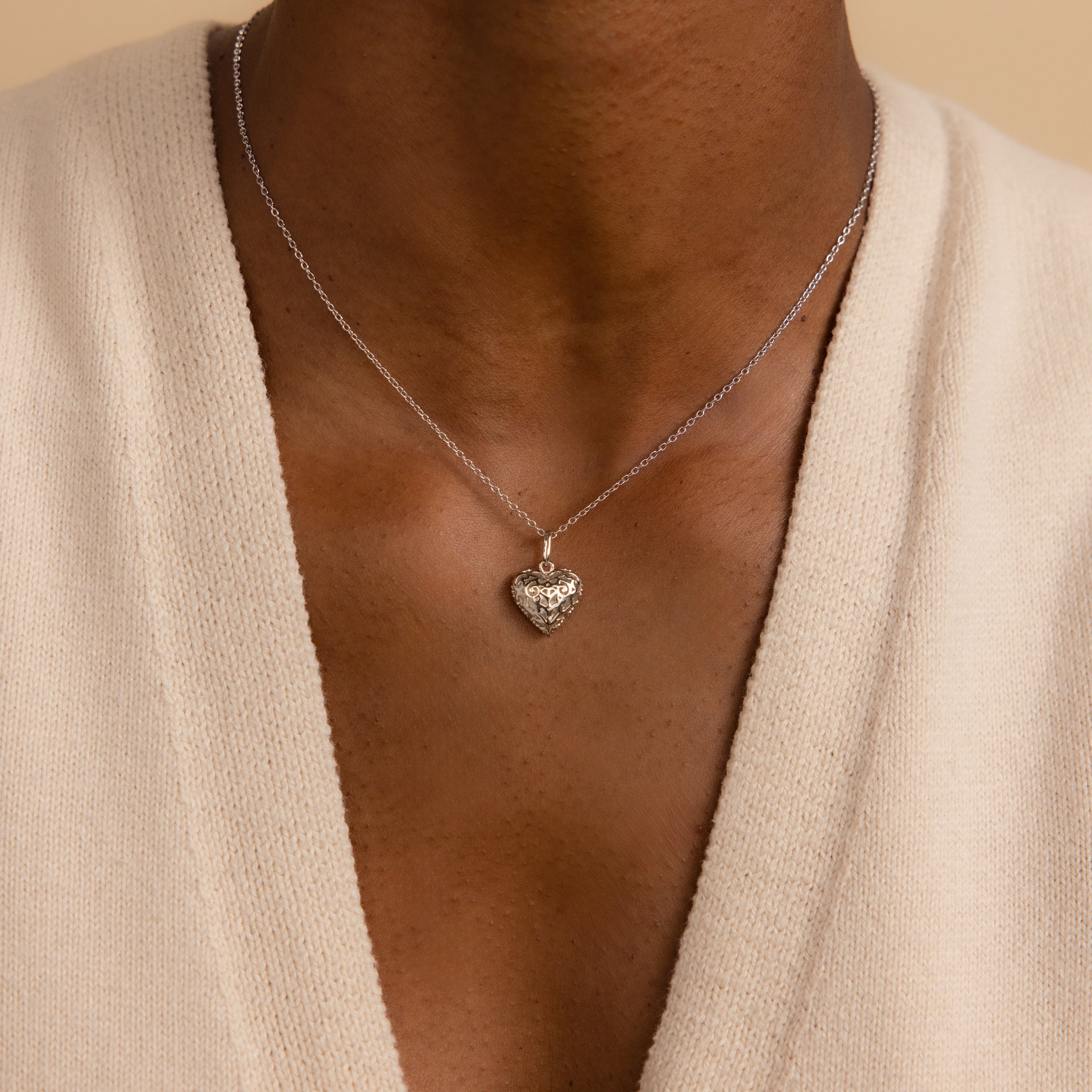 A person wearing the Vintage Heart Charm in Sterling Silver pendant necklace with a cream V-neck top—an elegant addition to any jewelry collection.