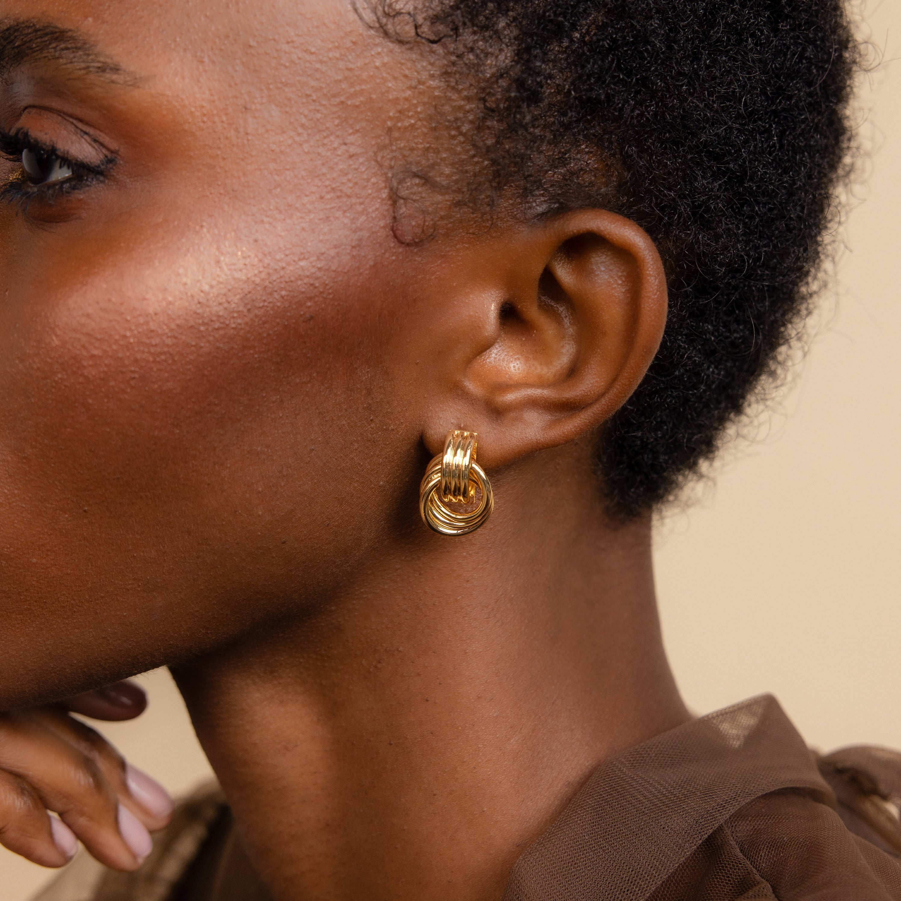 Close-up of a person with short hair wearing Triple Knot Earrings, hand under chin—the perfect elegant look for an anniversary gift.