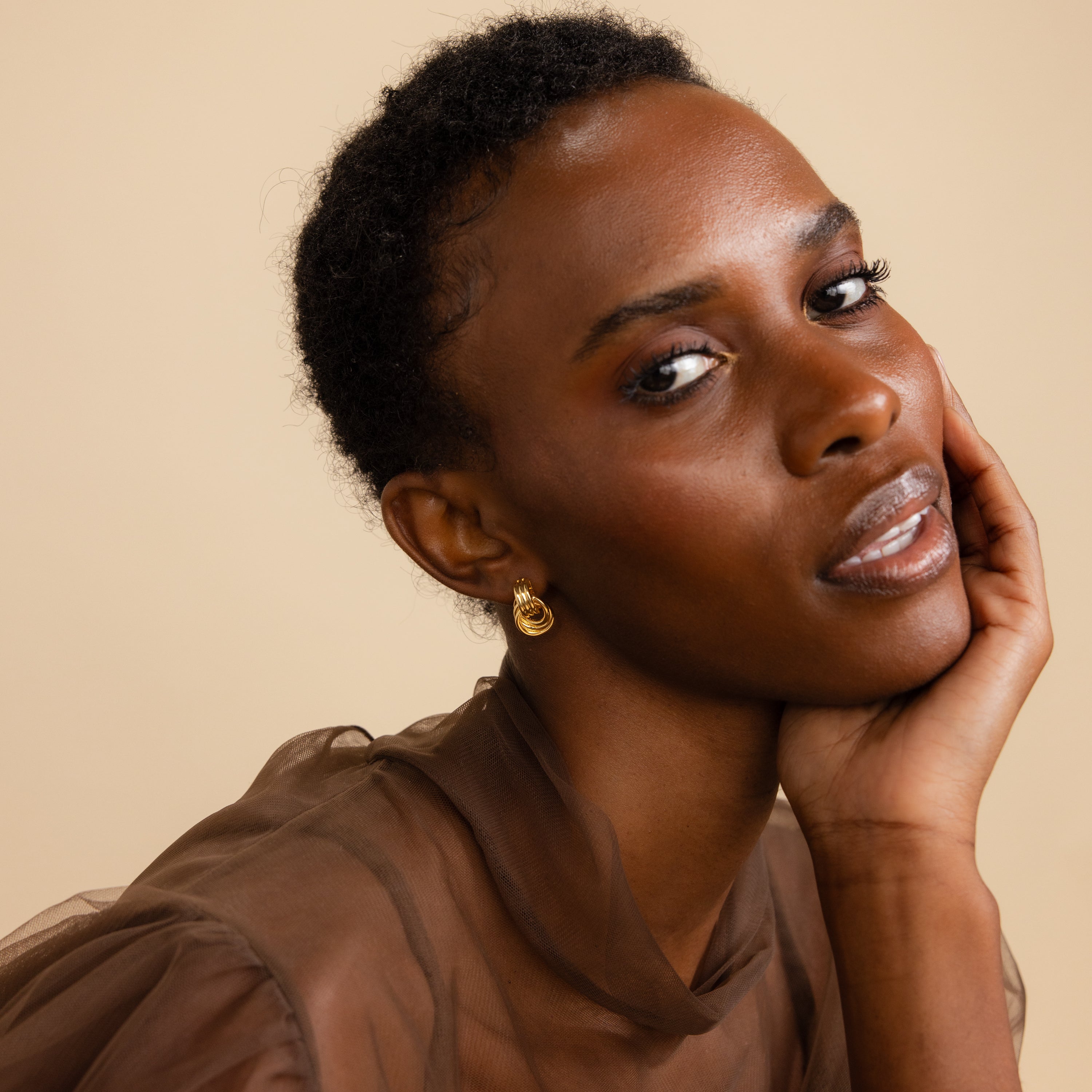 Portrait of a model smiling subtly and tilting her head, wearing a Mini Triple Knot Earring.