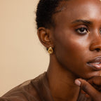 Portrait of a model gazing forward with a hand resting on her chin, wearing one Mini Triple Knot Earring on her left ear.