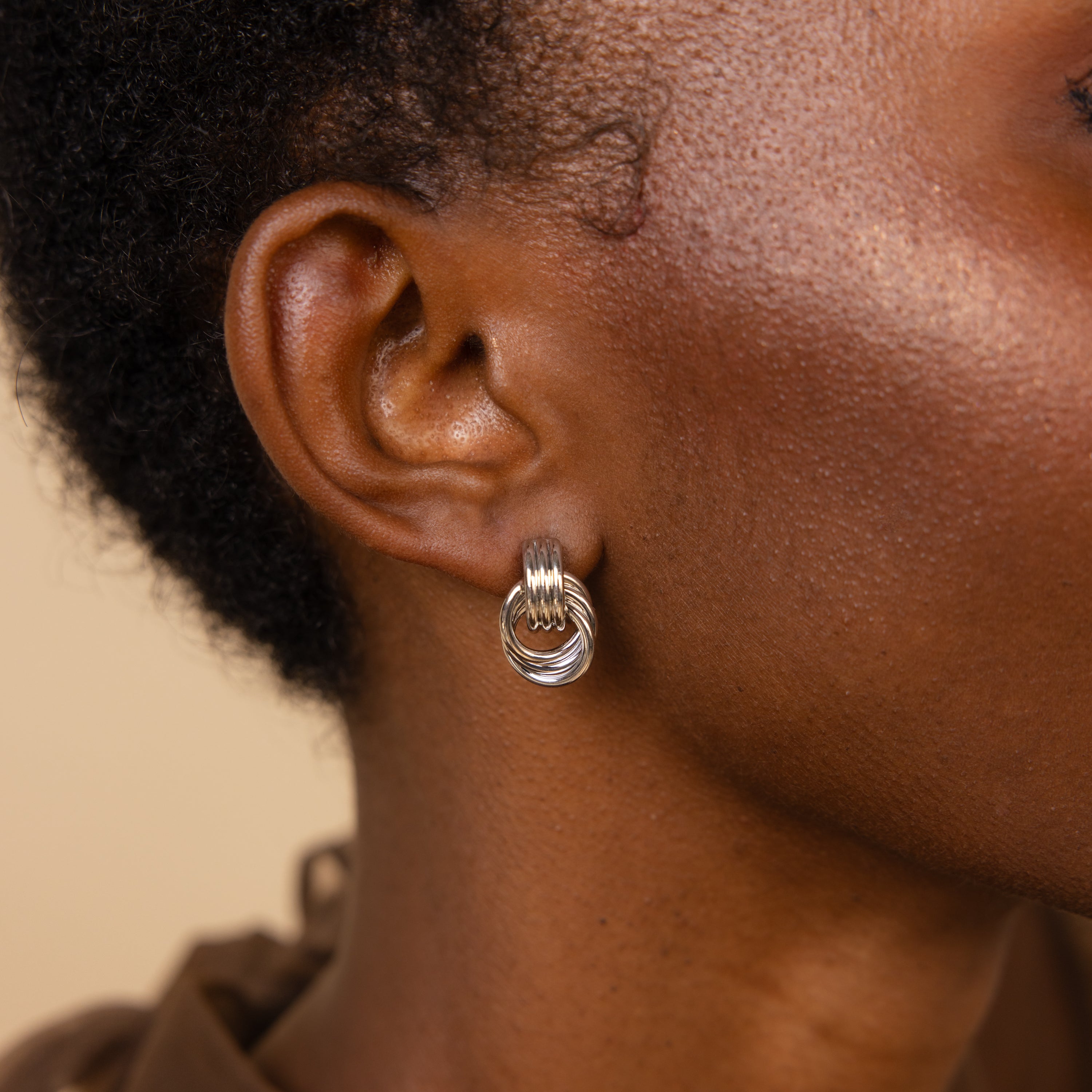 Close-up of silver Mini Triple Knot Earrings on a model’s ear.