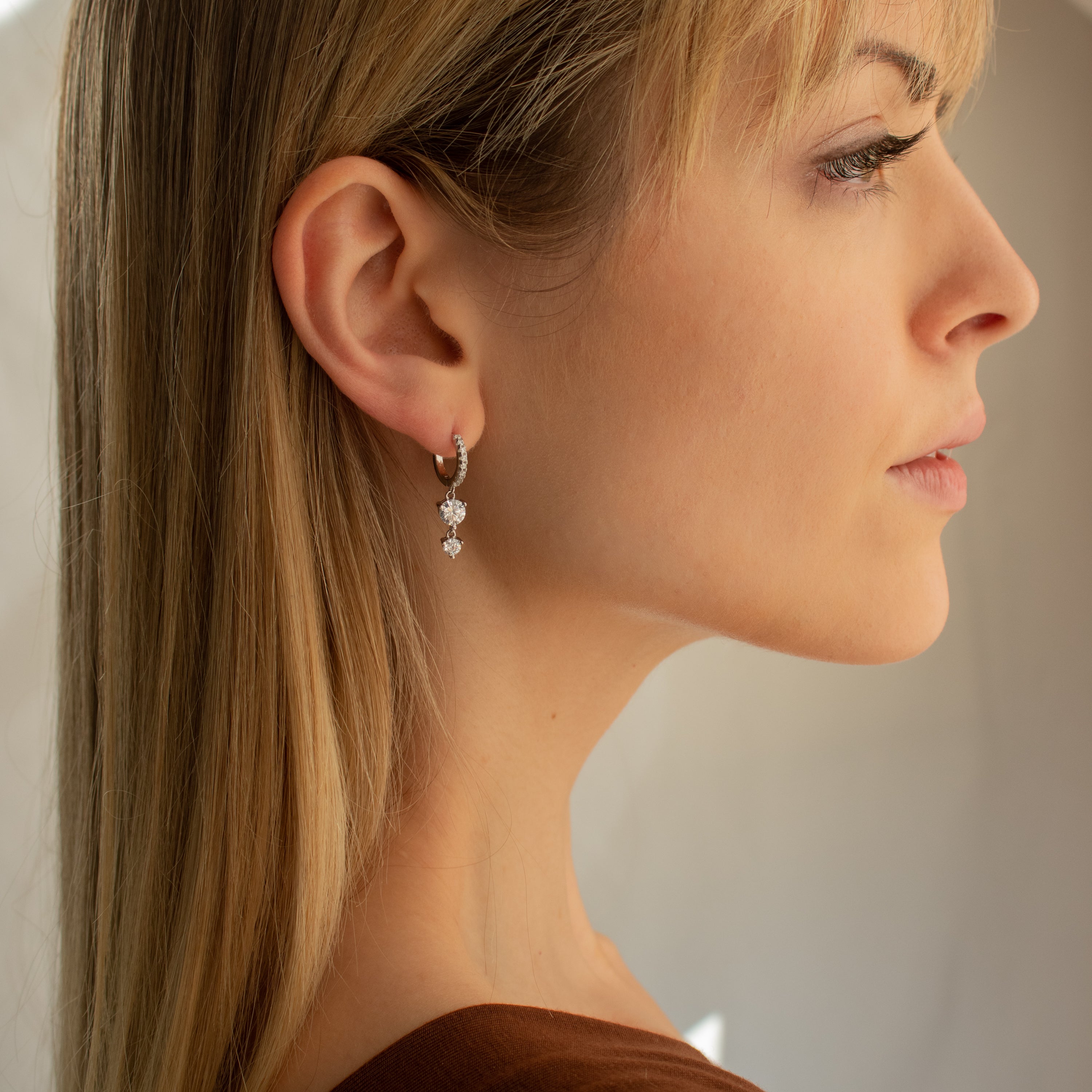 Blonde woman in profile wearing Caroline Pave Drop Huggies in Silver, gazing thoughtfully to the right.