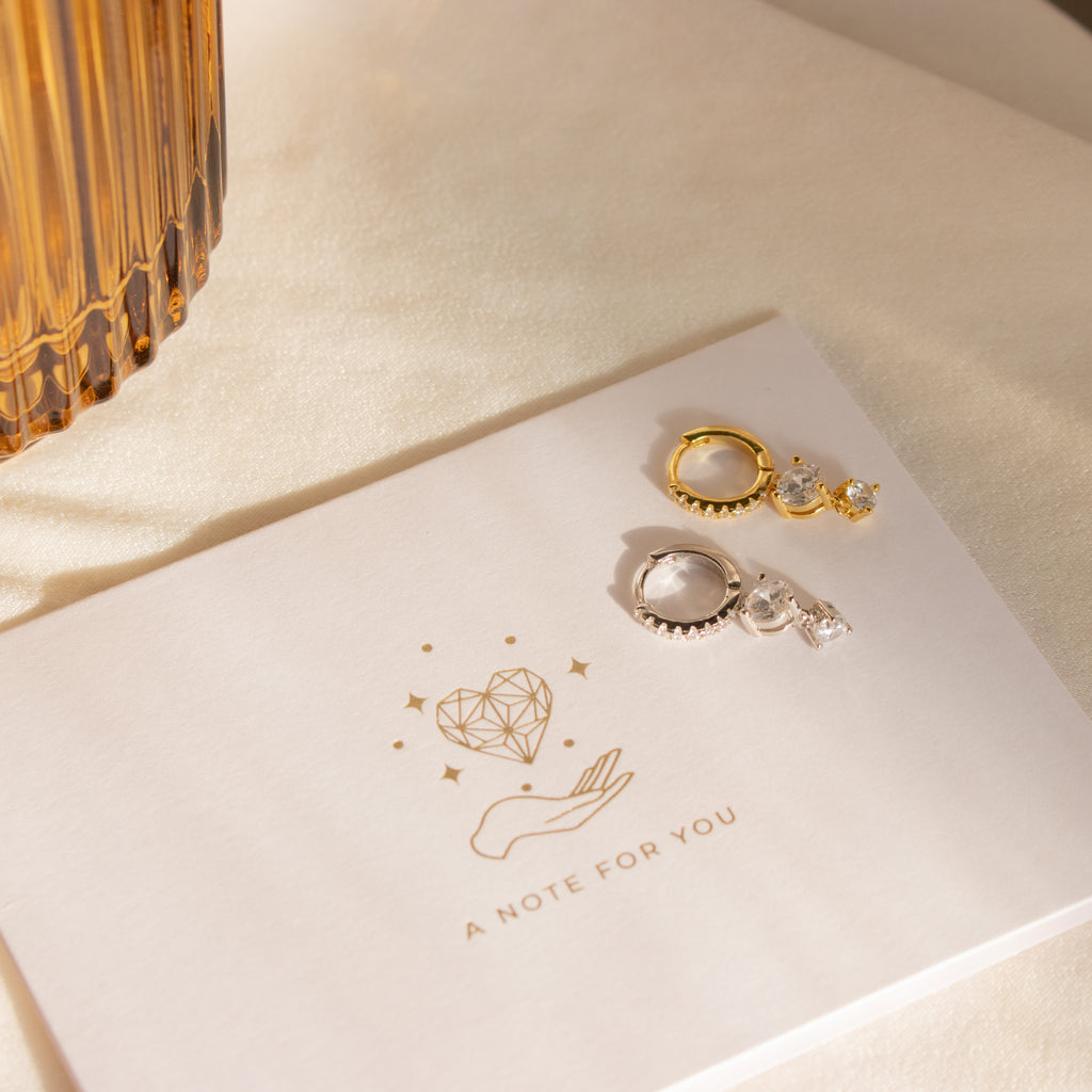 Caroline Pave Drop Huggies in Silver displayed on a card with heart and hand illustration, reading A NOTE FOR YOU.