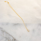 The Sage Diamond Necklace in 18K Gold features a delicate square pendant, radiating timeless elegance against a marble and fabric backdrop.