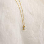 The Sage Diamond Necklace features a delicate gold chain with a rectangular clear gemstone pendant, elegantly displayed against a white fabric background.