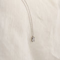 The Sage Diamond Necklace in Silver features a delicate chain and rectangular gemstone pendant, radiating timeless elegance against a soft cream fabric background.