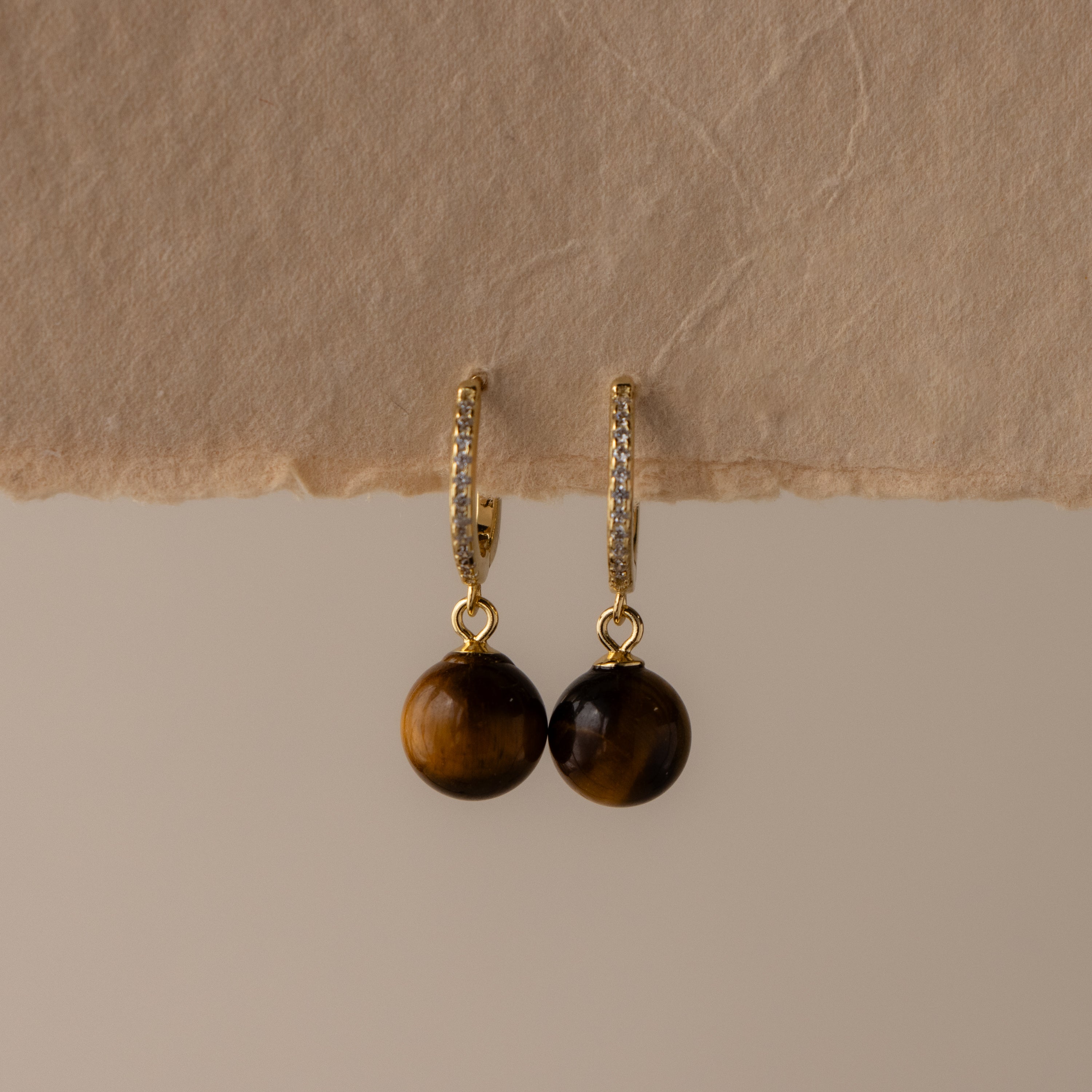 Pave Tiger's Eye Drop Huggies shown on a textured beige paper background.