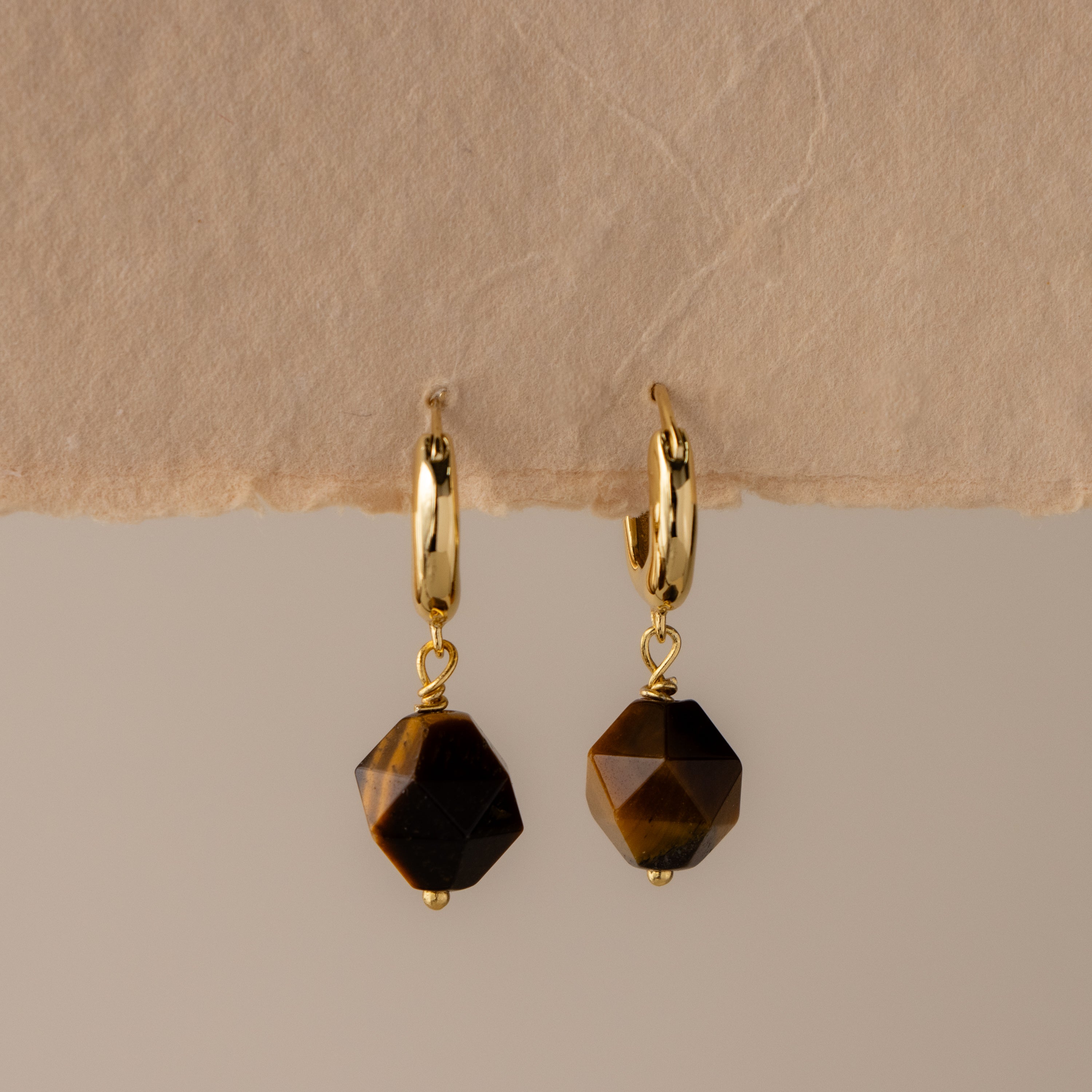 Geometric Tiger's Eye Drop Huggies with faceted brown gemstone dangles, displayed on a neutral textured background.