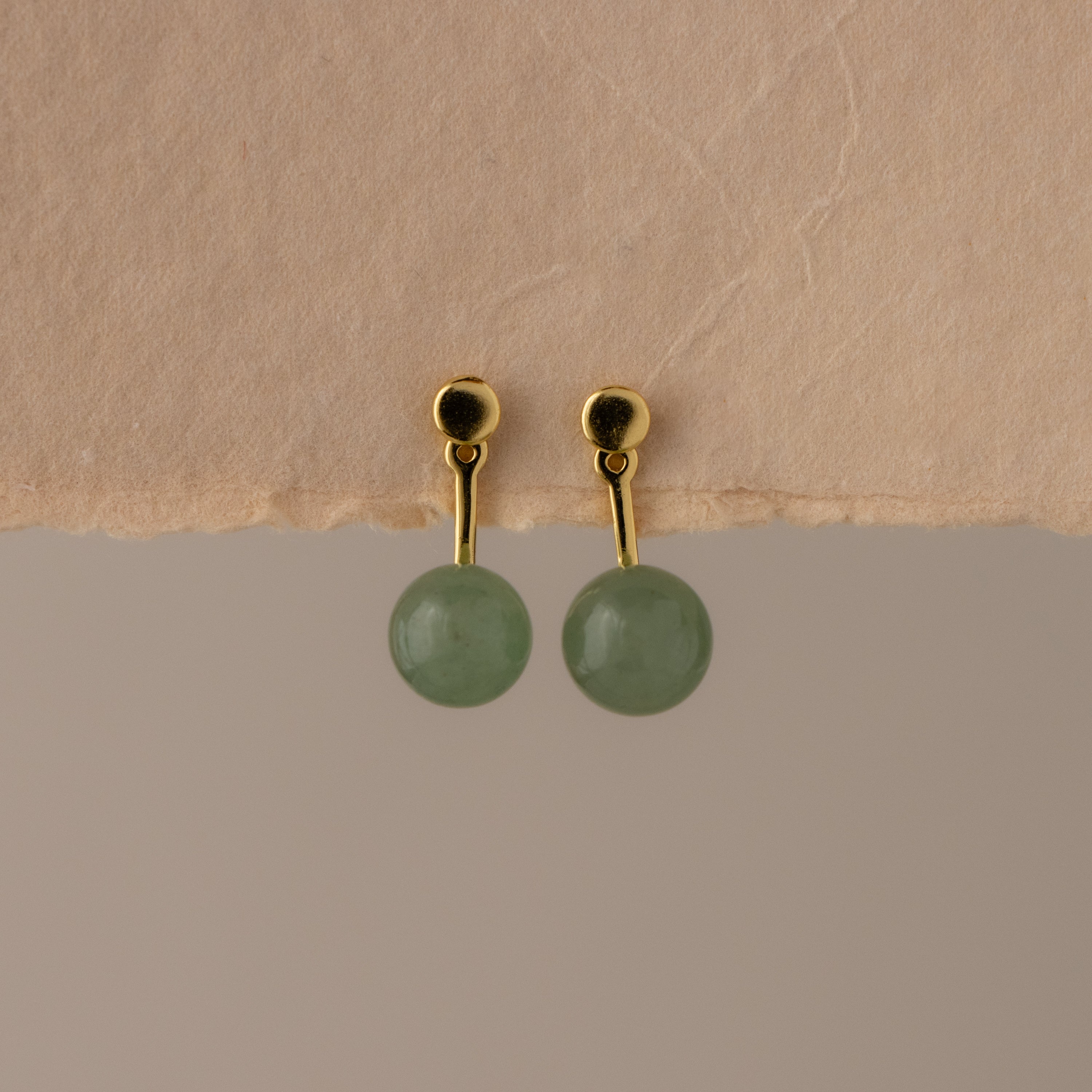Aventurine Bead Ear Jackets with green round gemstones, displayed on a textured beige surface.