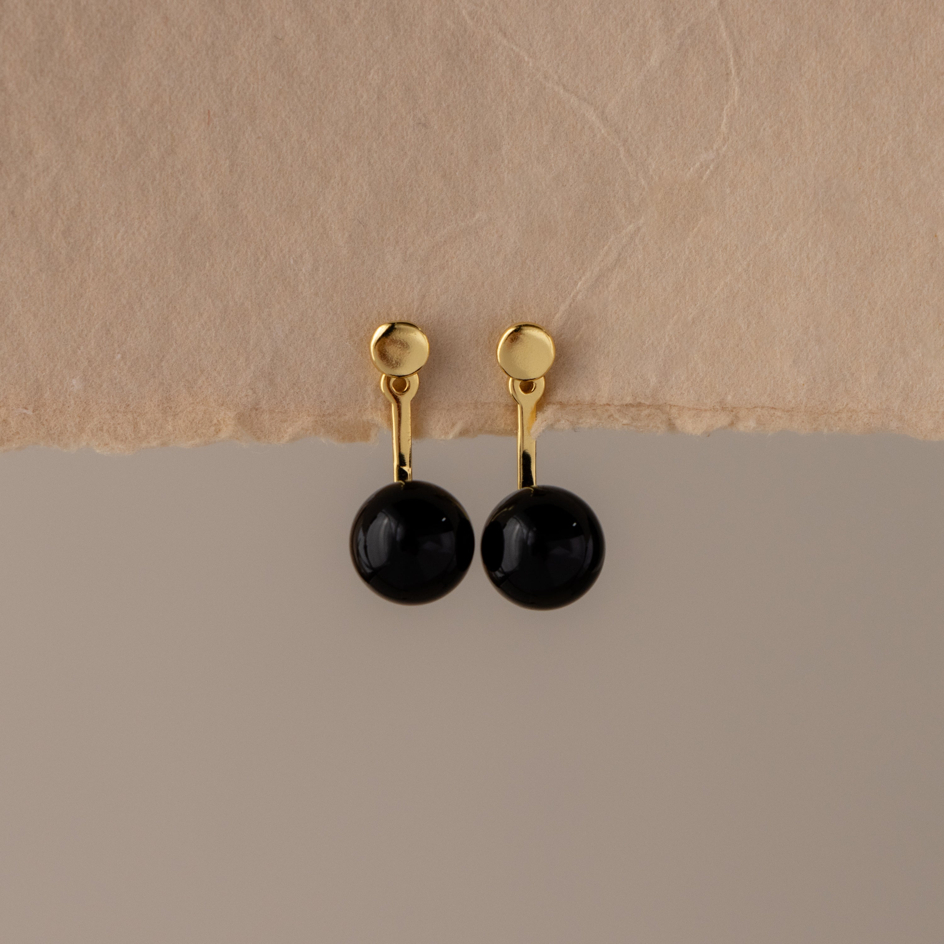 Onyx Bead Ear Jackets featuring round black stones, displayed against a neutral background with a textured surface.