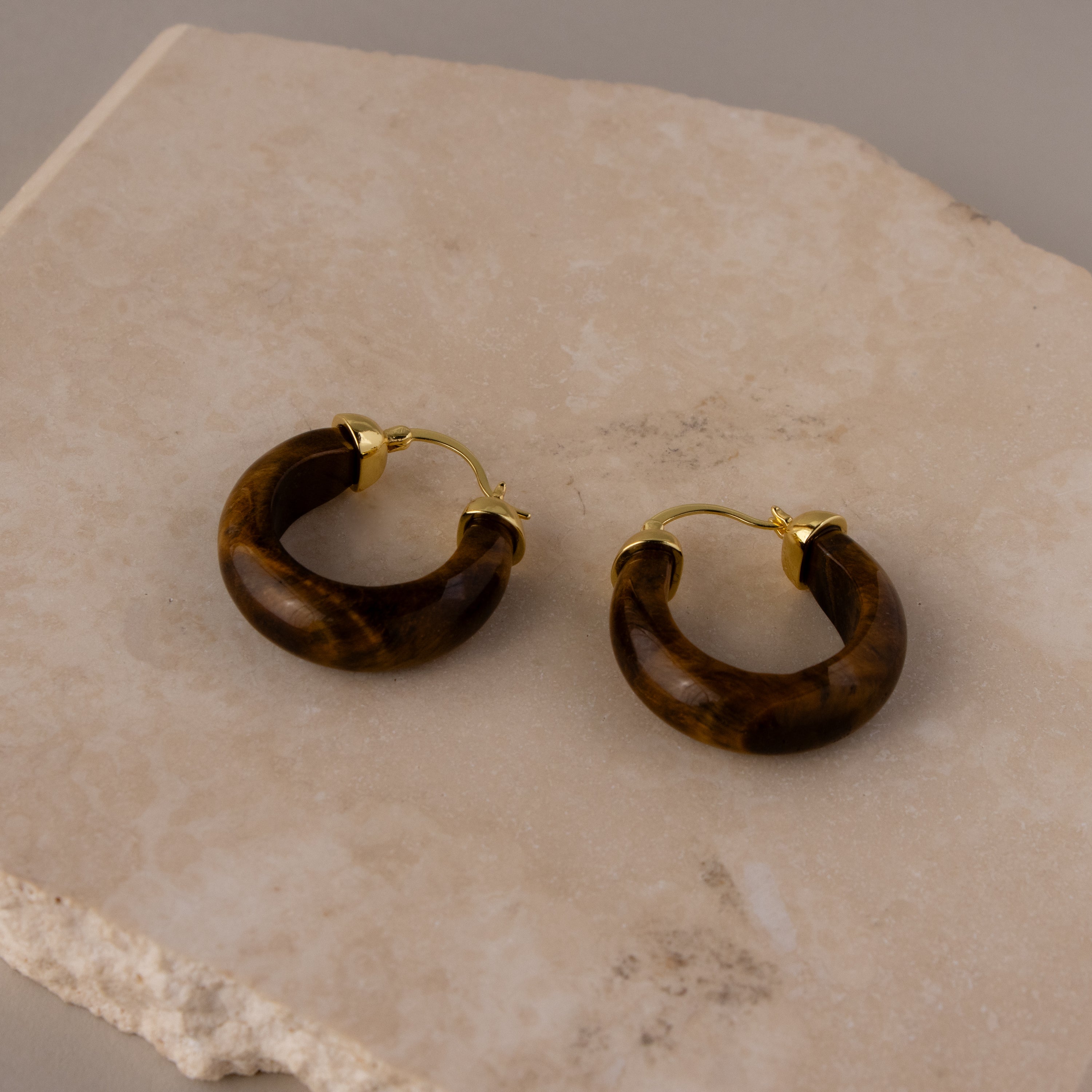 Small Tiger's Eye Hoops with gold clasps displayed on a beige stone surface.