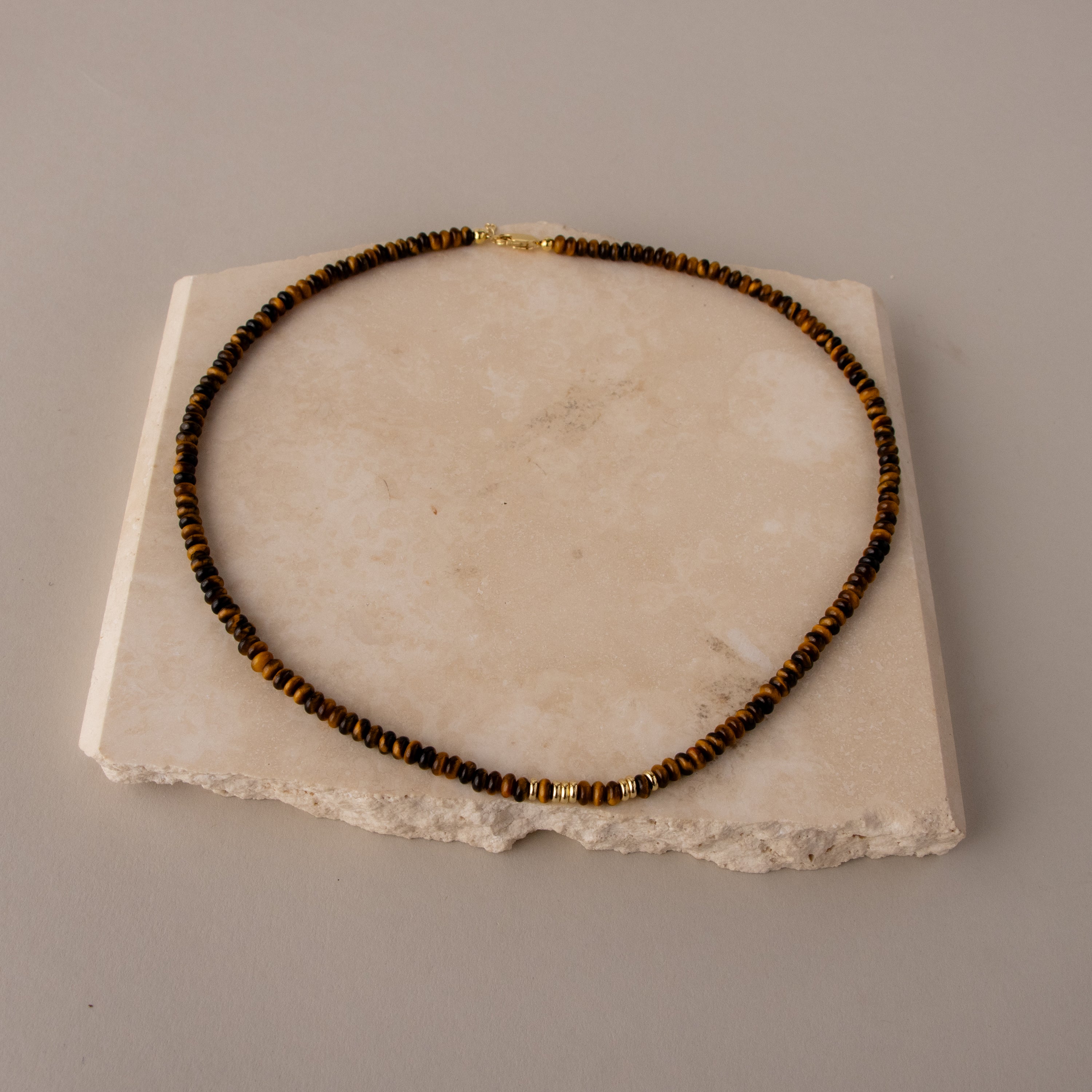 Love Code Beaded Tiger Eye's Chain featuring brown and gold beads, displayed on a rough, square stone slab.