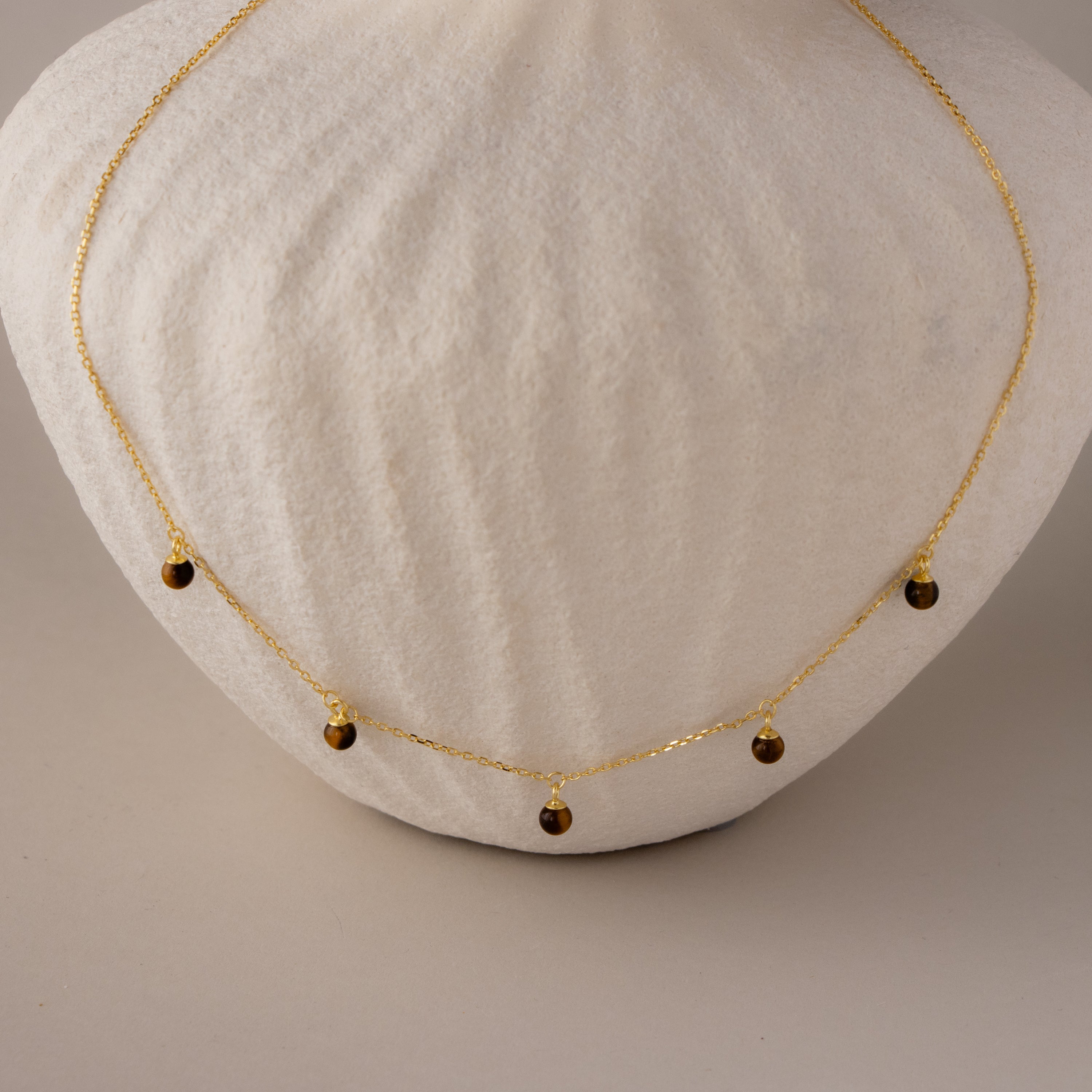 Tiger's Eye Beaded Dome Station Necklace featuring five small brown teardrop pendants, beautifully displayed on a white textured surface.