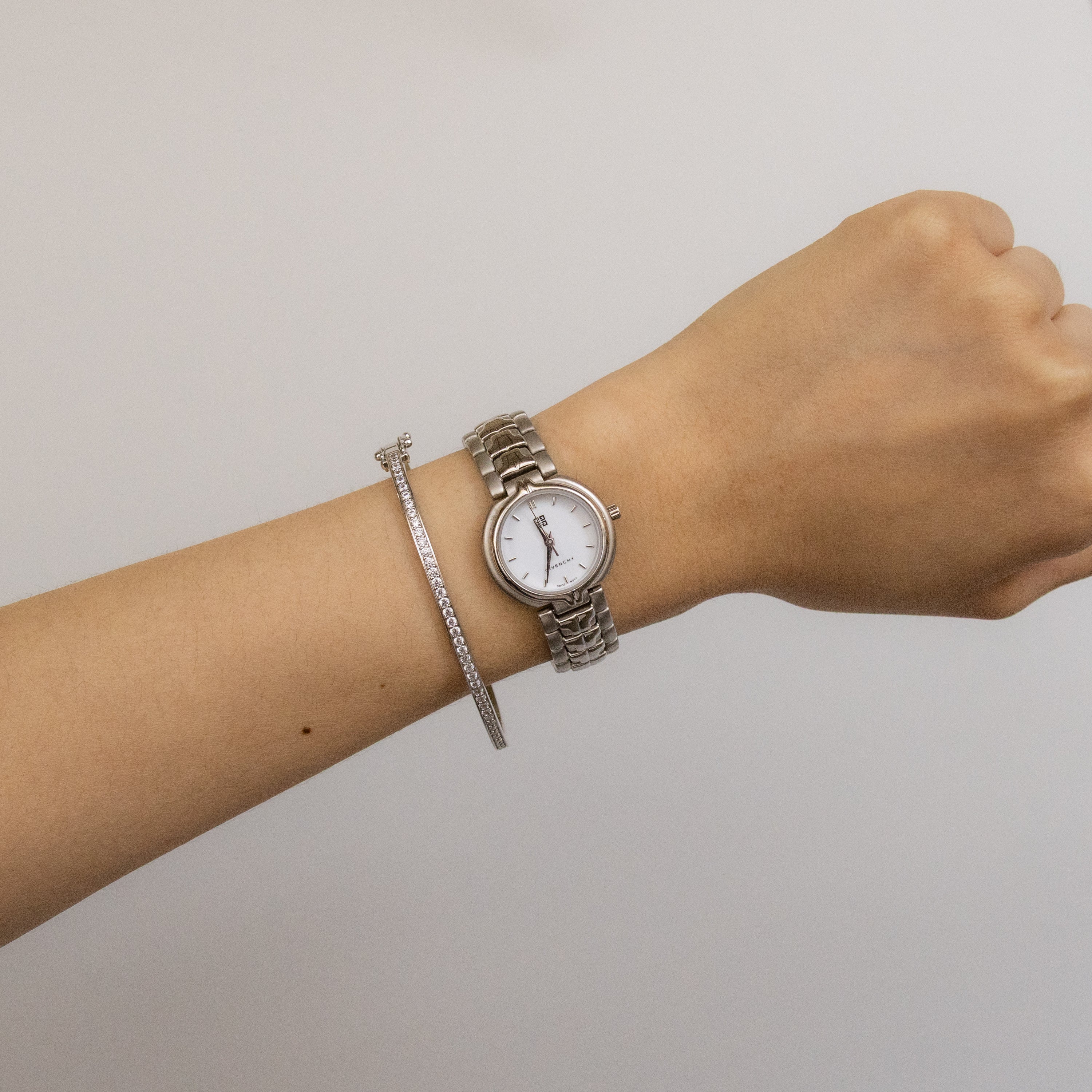 A wrist adorned with the Vintage Givenchy Swiss Bold Silver Watch and a slim silver bracelet against a light background, creating an understated yet striking statement piece.