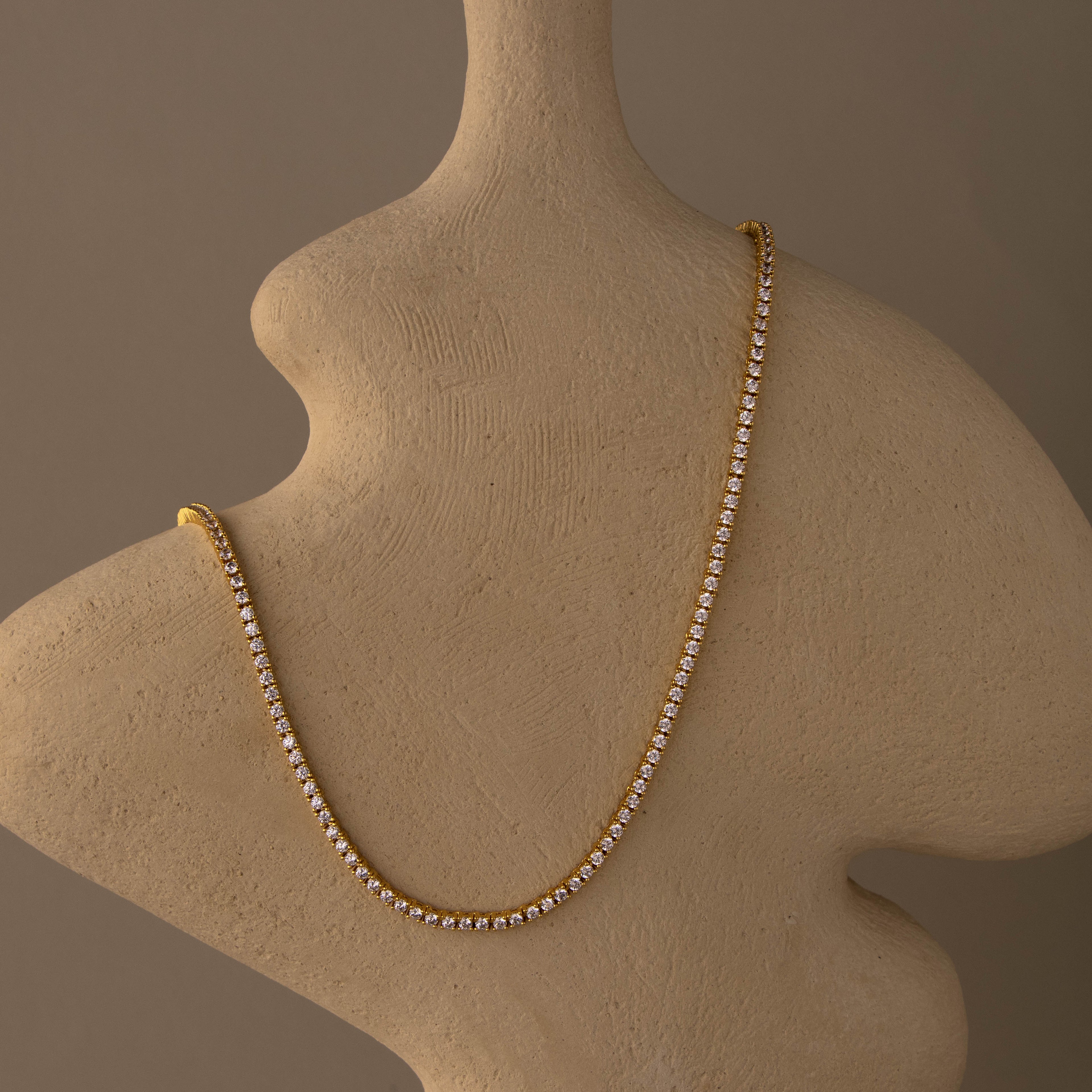 The 2.5mm Diamond Tennis Necklace is displayed draped over a beige, smooth, curved abstract sculpture.
