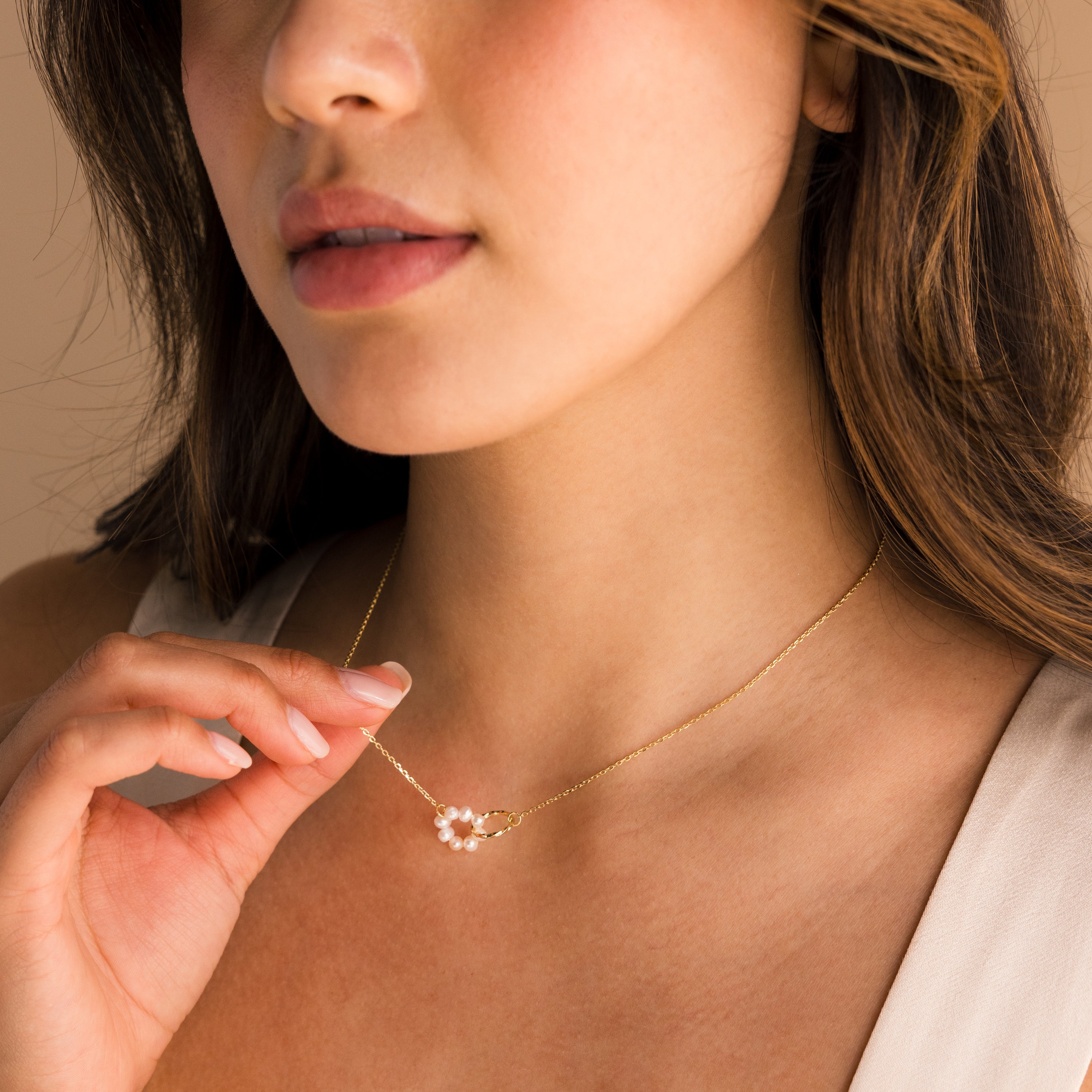 A woman gently holds the Interlocking Pearl Necklace, featuring an interlocking pearl pendant, near her neck.