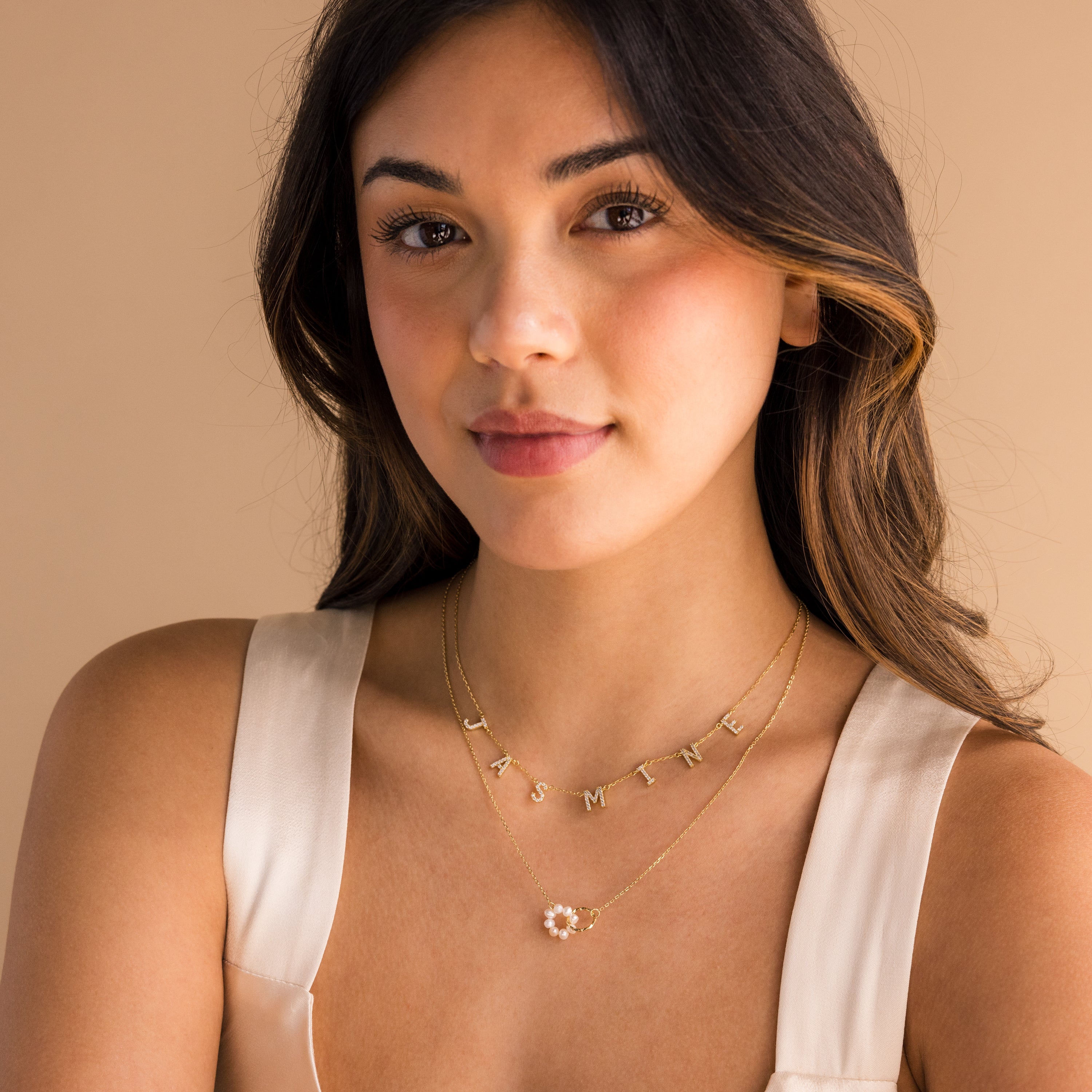 Woman with long brown hair wearing a cream top and layered gold necklaces, including the Interlocking Pearl Necklace.