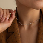 A person in a brown blazer holds the Dainty Marquise Pendant Necklace, featuring a small marquise-cut diamond and a mirror twist chain, near their neck.