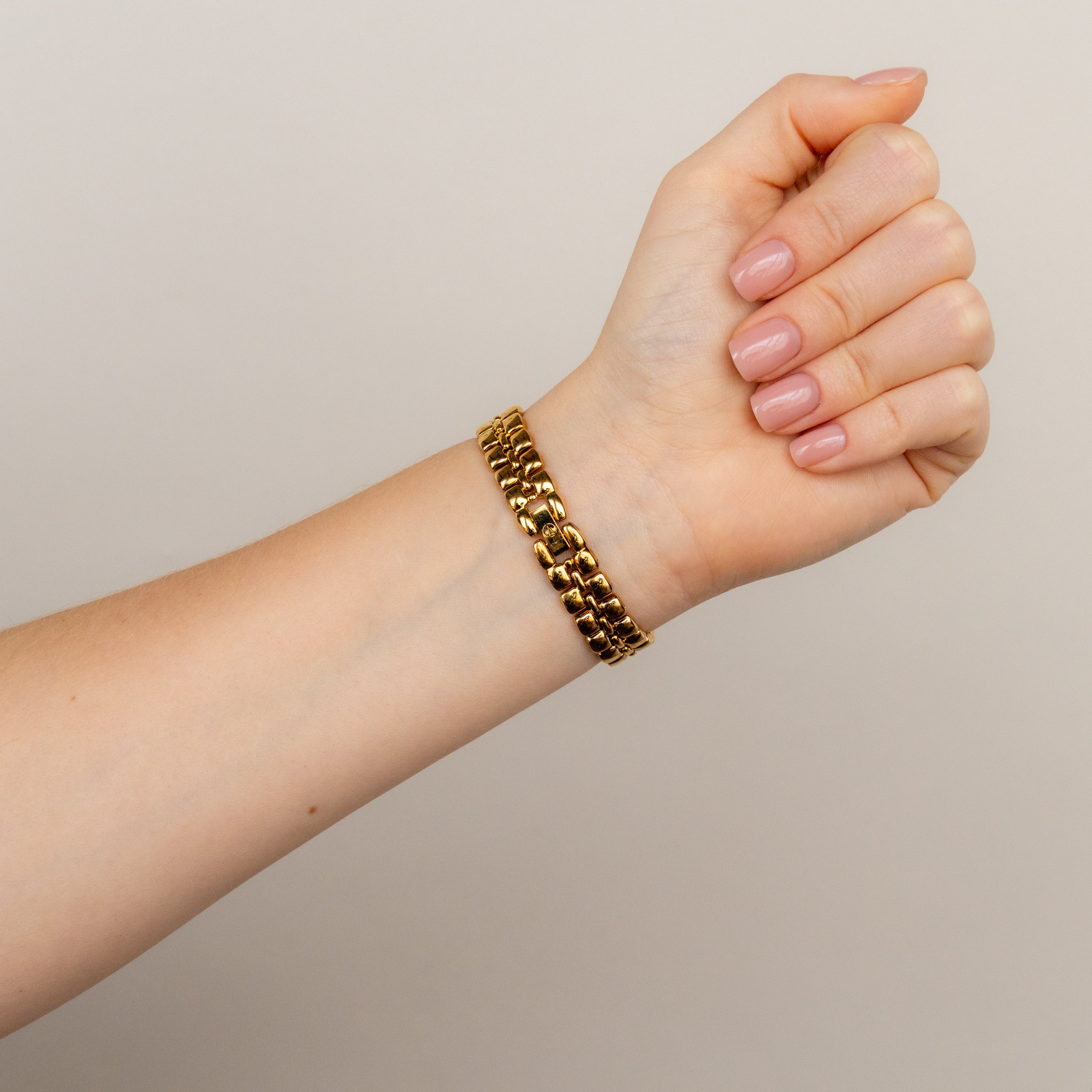 A hand with neatly manicured nails wears a gold link bracelet and the Vintage La Tour Eiffel Round Gold Watch, posed against a plain background.