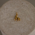 Dainty Horse Charm pendant displayed on a textured beige stone surface.