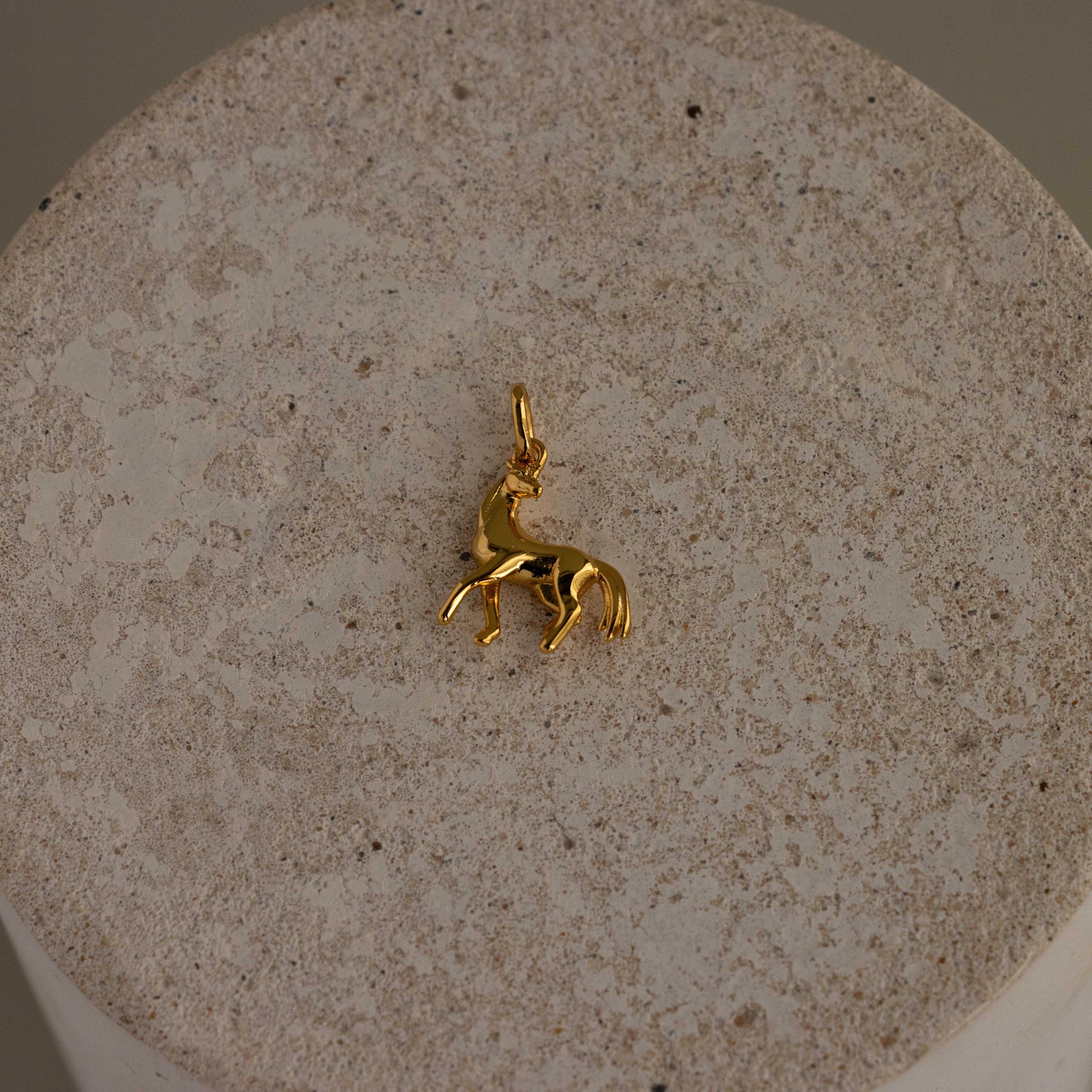 Dainty Horse Charm pendant displayed on a textured beige stone surface.