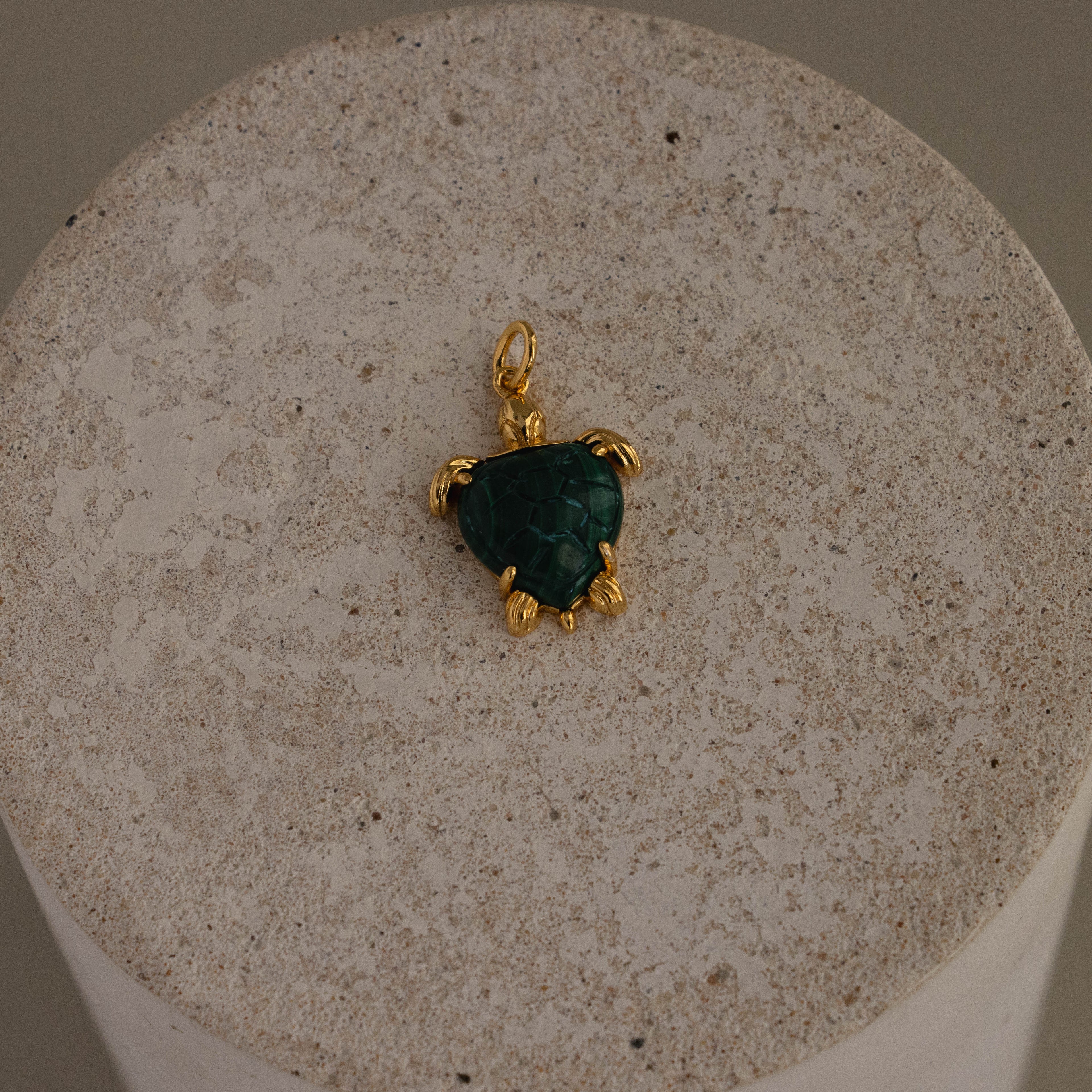 Malachite Sea Turtle Charm with a green stone shell, shown on a round textured beige surface.