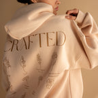 A person wearing an Oversized CM Hoodie in beige, featuring CRAFTED and flower prints on the back—ideal for fans of Caitlyn Minimalist style.