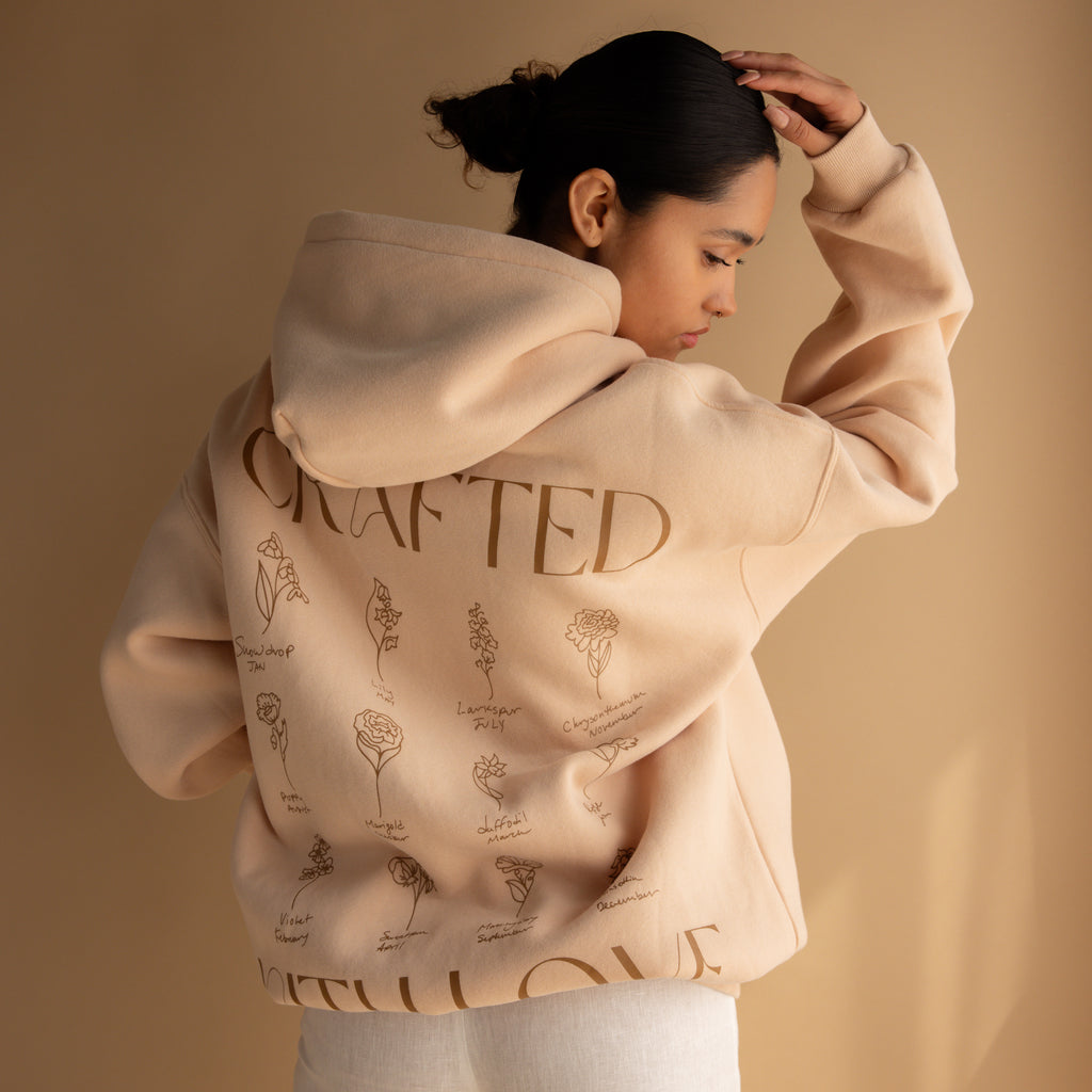 Model wears the Oversized CM Hoodie, featuring floral designs and back text, set against a beige background.
