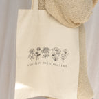 The CM Tote Bag features chic beige fabric with floral line drawings and "caitlyn minimalist" text on the front—a versatile accessory ideal for everyday style.