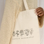 A person carries the CM Tote Bag in cream, adorned with floral line art and the text "caitlyn minimalist.