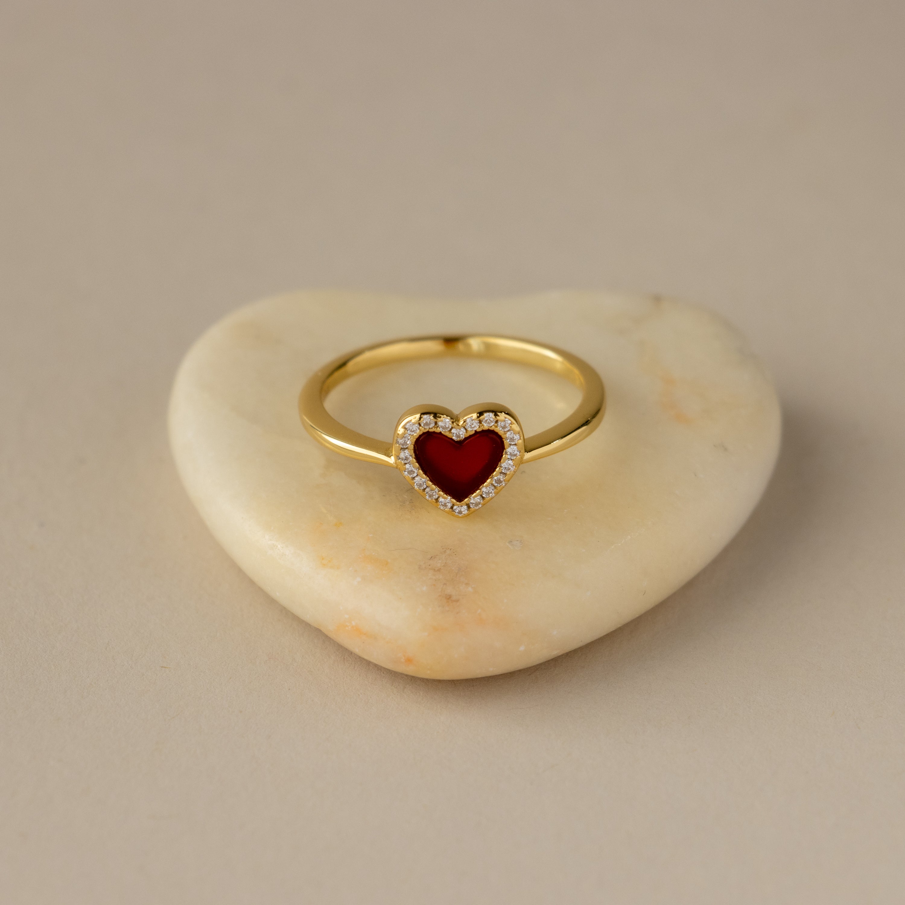 The Red Agate Pave Heart Ring features a red heart-shaped center and small diamonds, elegantly displayed on a heart-shaped stone.