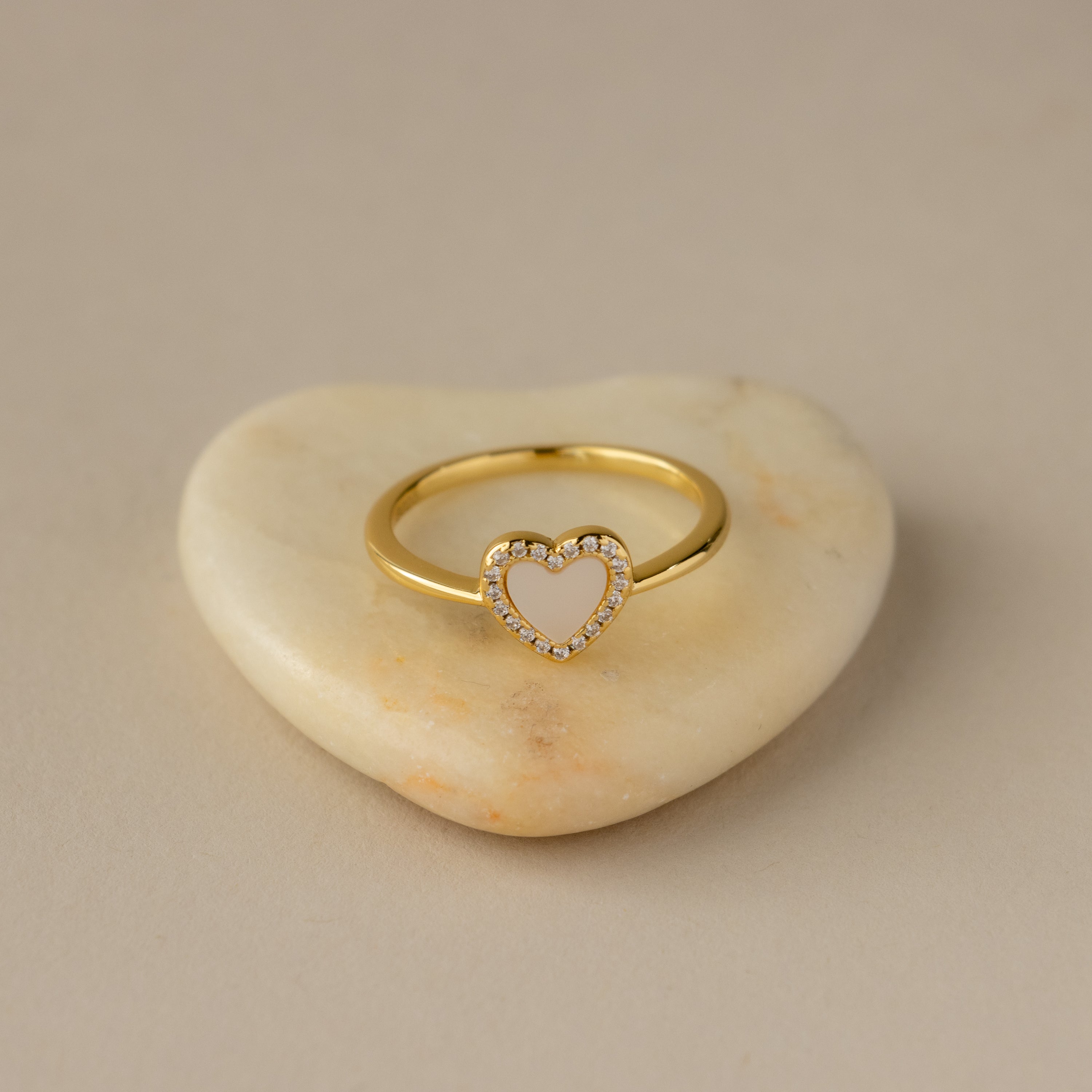 The Mother of Pearl Pave Heart Ring features a heart-shaped center with sparkling accents, elegantly displayed on a heart-shaped stone.