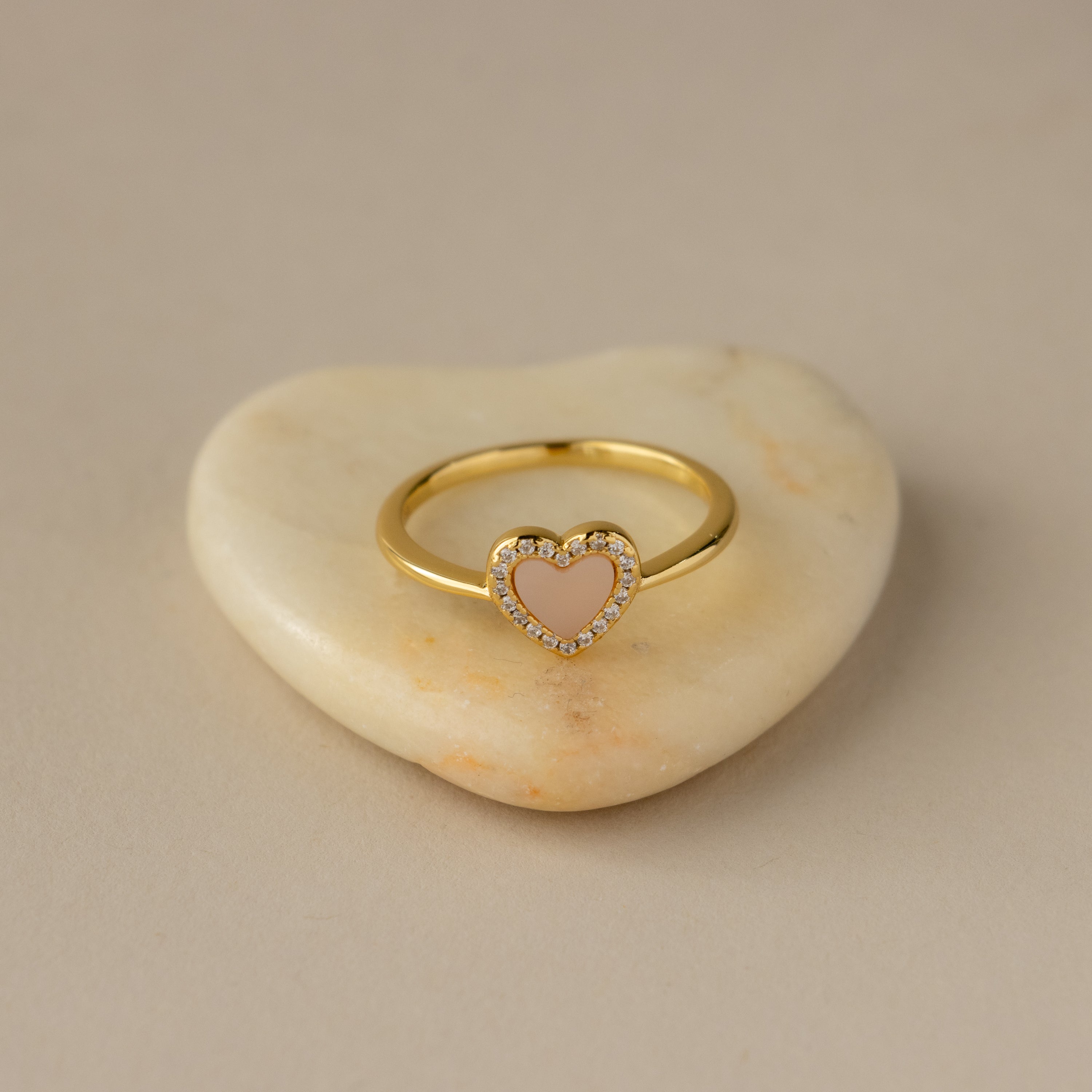 The Pink Pave Heart Ring features a pink heart-shaped center with sparkling crystals, displayed on a heart-shaped stone.