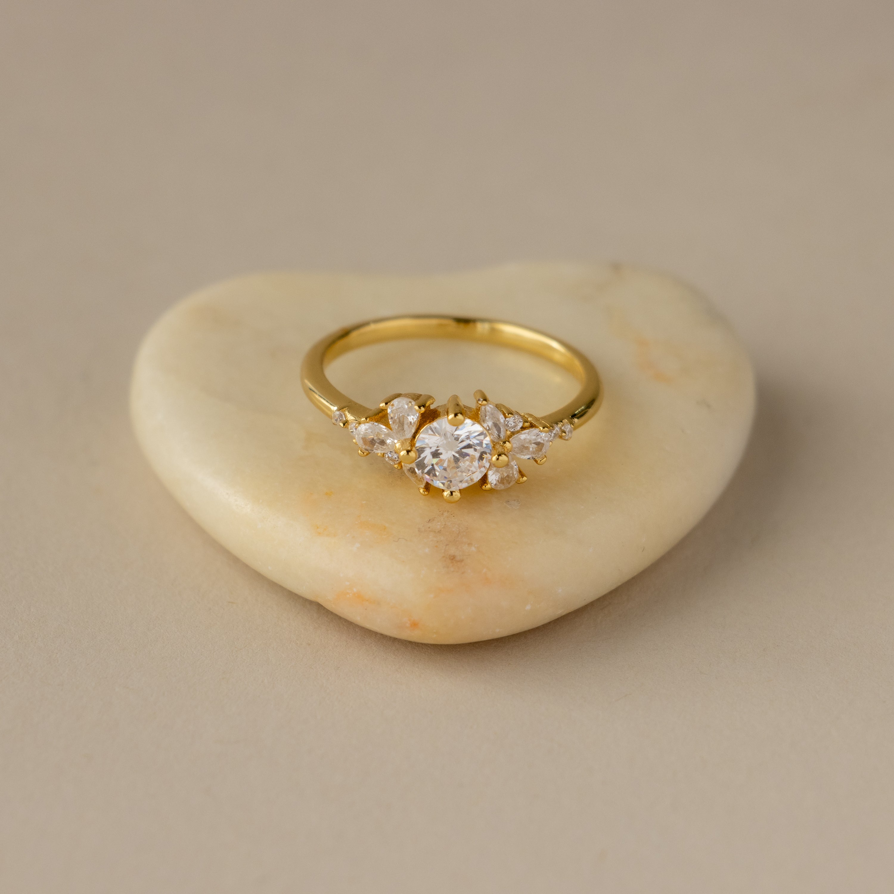 Round Stone Petal Diamond Ring featuring a prominent central diamond and smaller side stones, elegantly displayed on a smooth, heart-shaped stone.