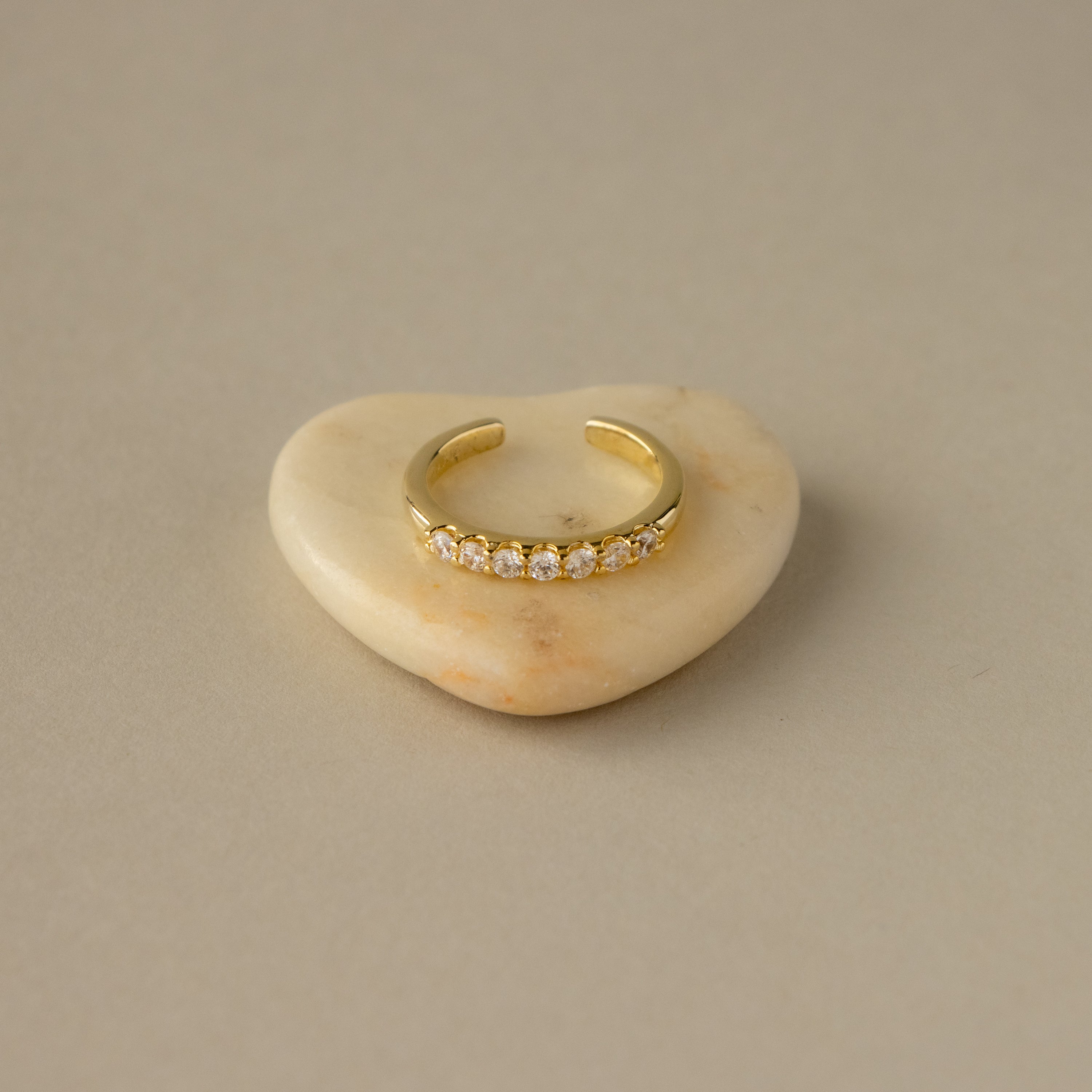 Open Round Diamond Ring with sparkling diamonds, shown on a smooth, heart-shaped beige stone background.