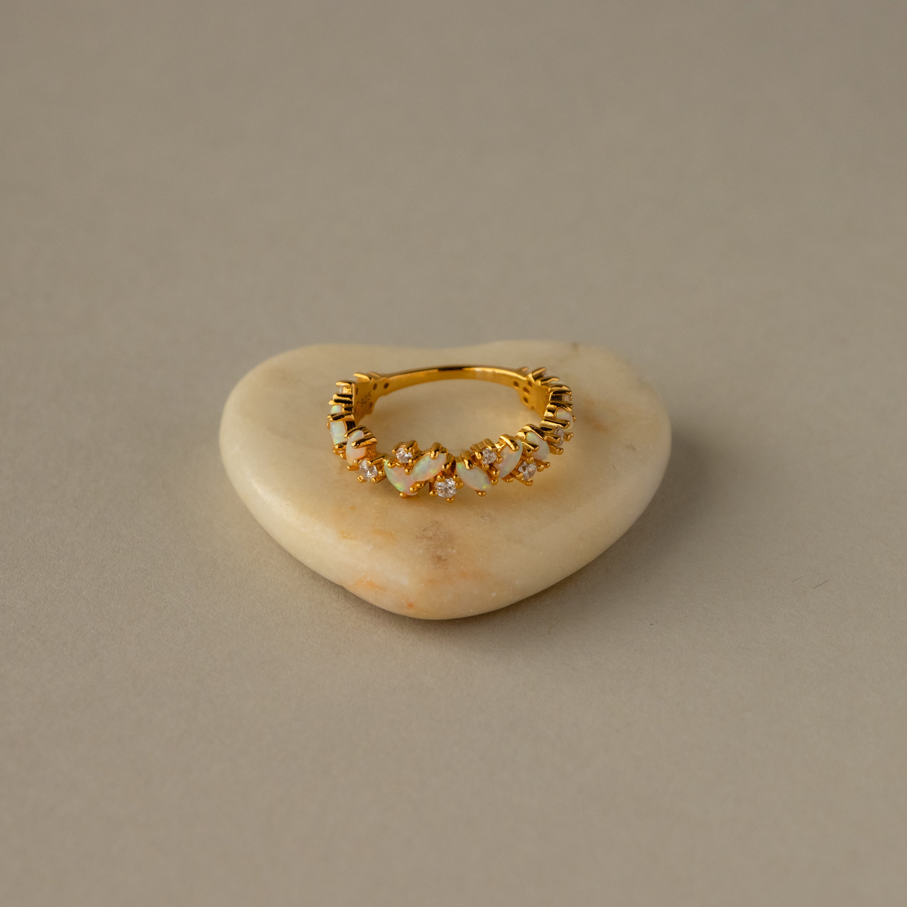 The Diamond Marquise Opal Cluster Ring sits on a smooth, heart-shaped stone, displayed against a beige background.