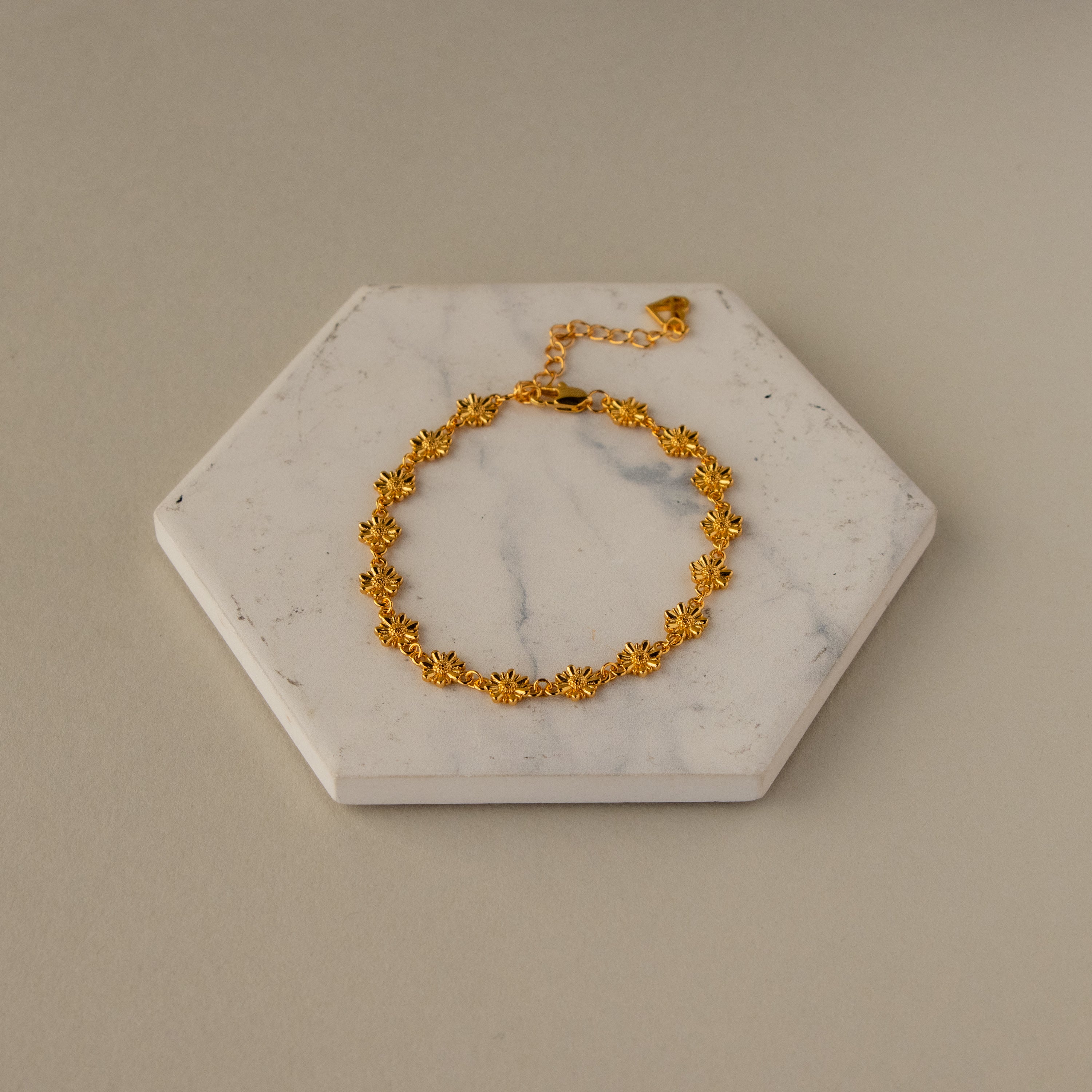 The Daisy Link Charm Bracelet is shown on a hexagonal white marble slab against a neutral background.