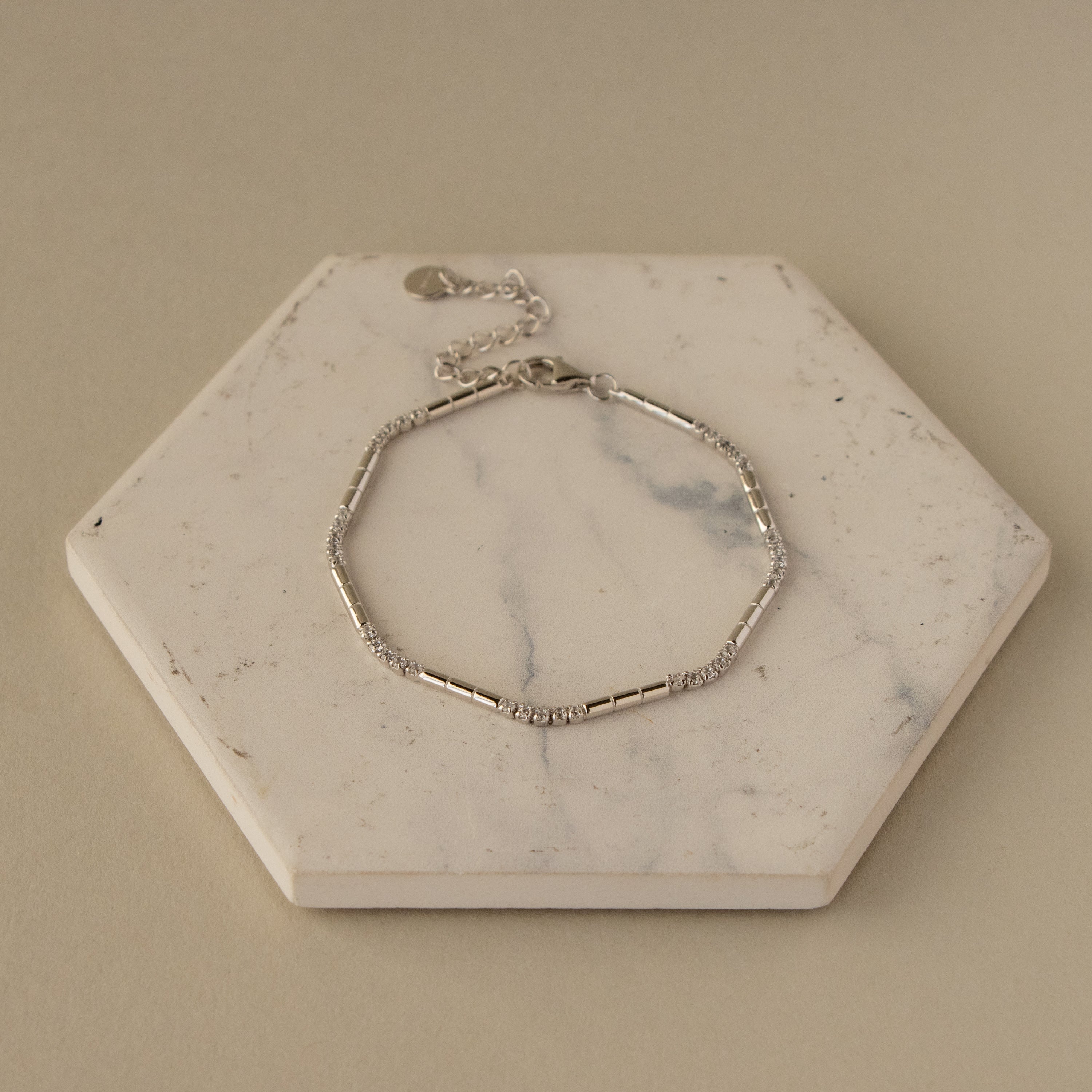 The Silver Diamond Dot & Dash Bracelet features a delicate silver chain with small beads, displayed on a hexagonal white marble slab.
