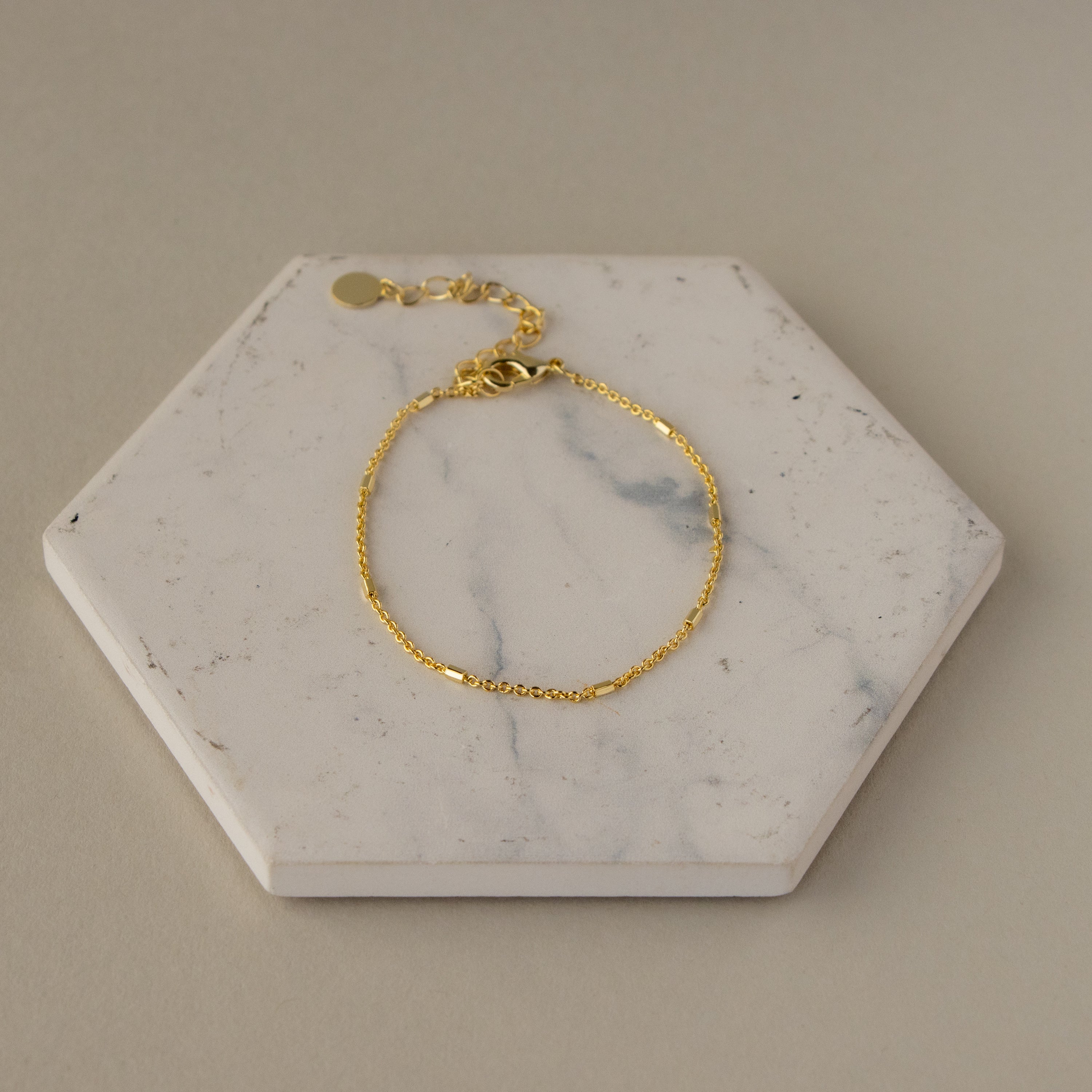 The Mini Bar Cable Chain Bracelet is displayed on a hexagonal white marble tile with a beige background.