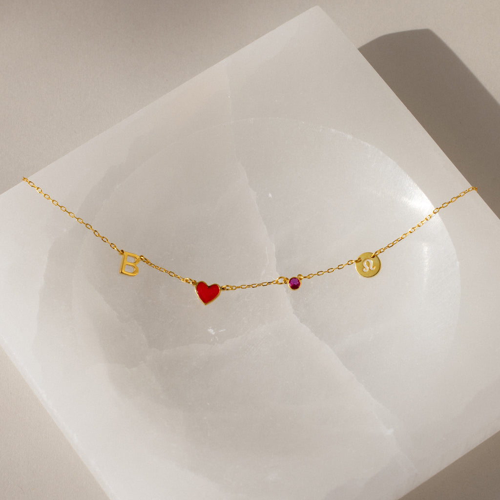 Gold bracelet with letter B, red heart, pink gem, and gold disc on a white square—perfect for pairing with the Dainty Space Charm Necklace or other customizable charm necklace styles.
