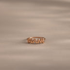 Up close of a dainty rose gold bubble letter ring with the name "DIANE" displayed on a neutral surface.