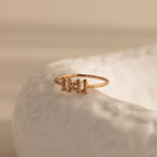 A close-up of a rose gold Bubble Numbers Ring featuring the number “11 11” in bold, rounded numerals, styled on the edge of a glossy, textured white ceramic surface with soft beige lighting.