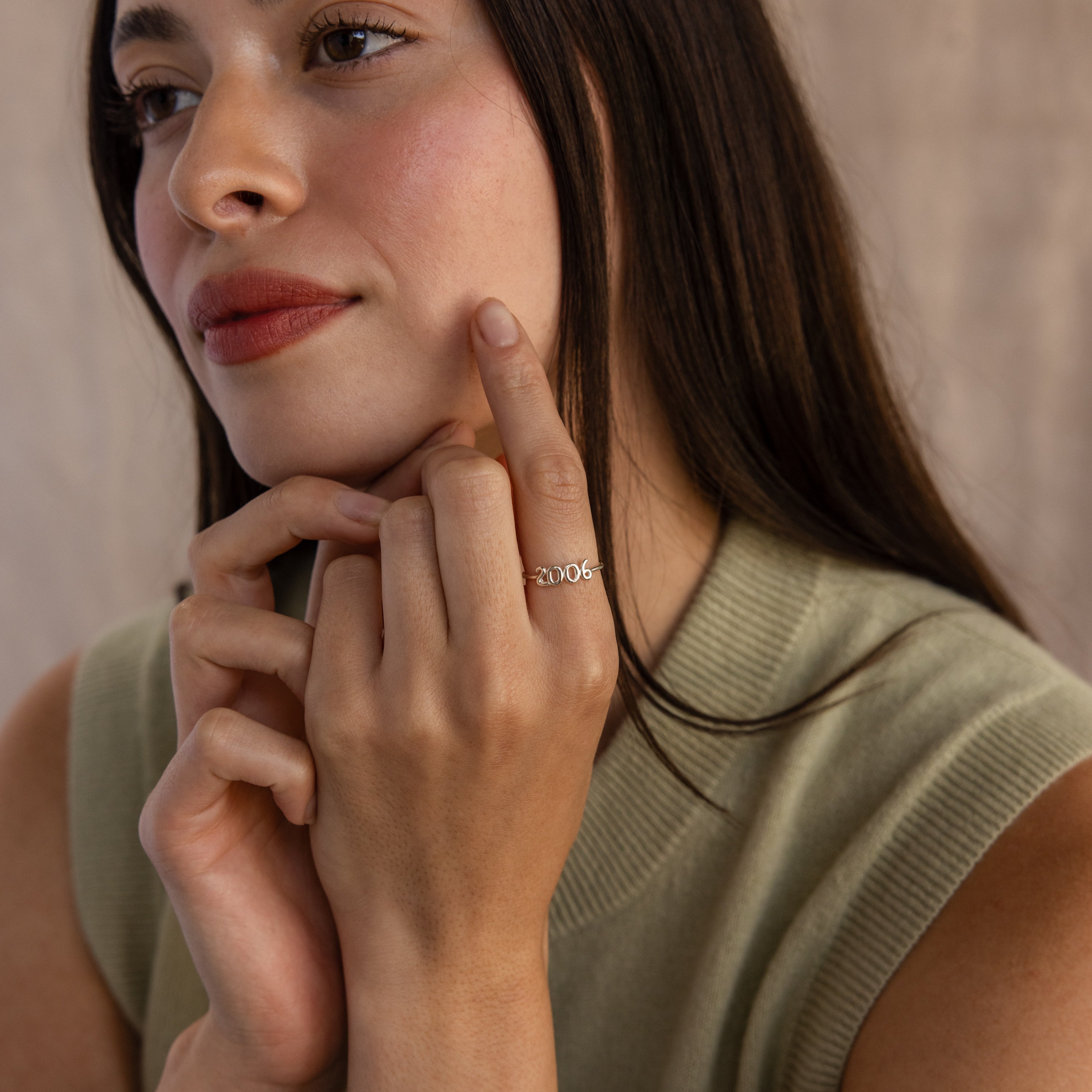 A woman showcases a silver Bubble Numbers Ring engraved with “2006” on her index finger, styled in a calm and minimal setting.