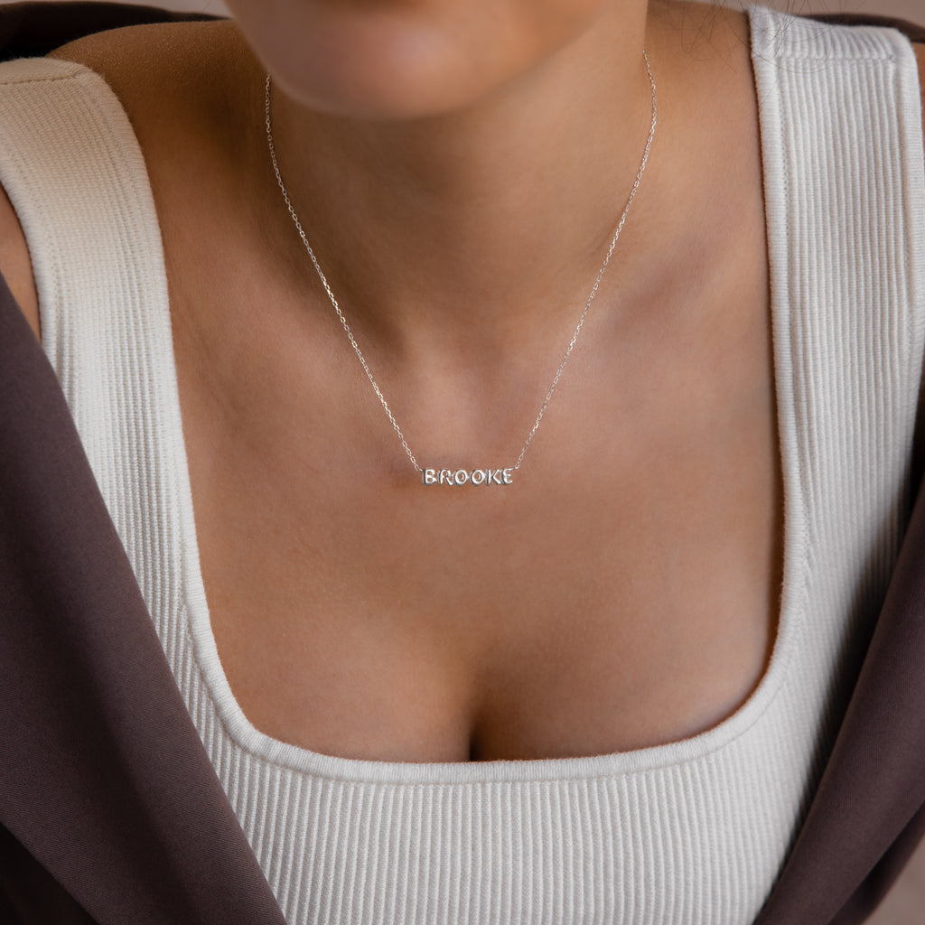 Model wears a dainty silver bubble name plate necklace that reads Brooke