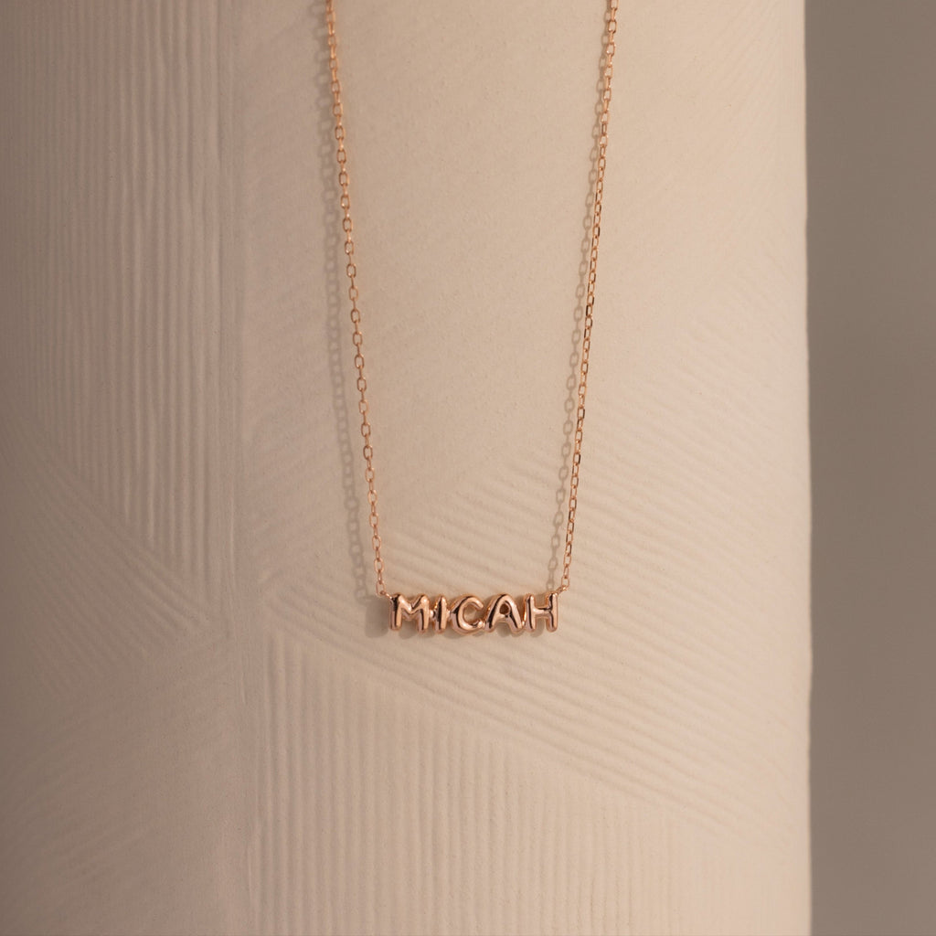 Dainty rose gold bubble name plate necklace with the name Micah, displayed against a neutral background.