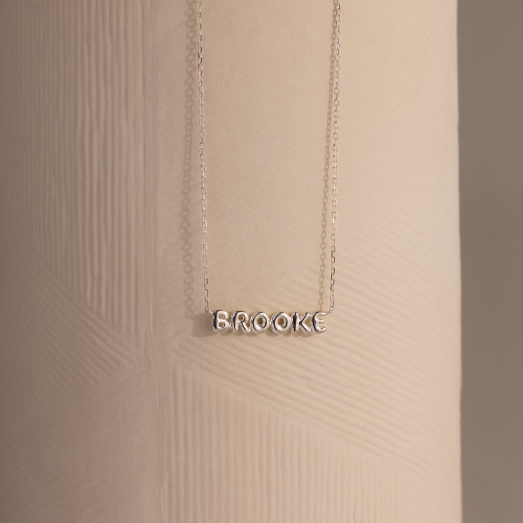 Dainty silver Brooke bubble name plate necklace displayed against a neutral surface.