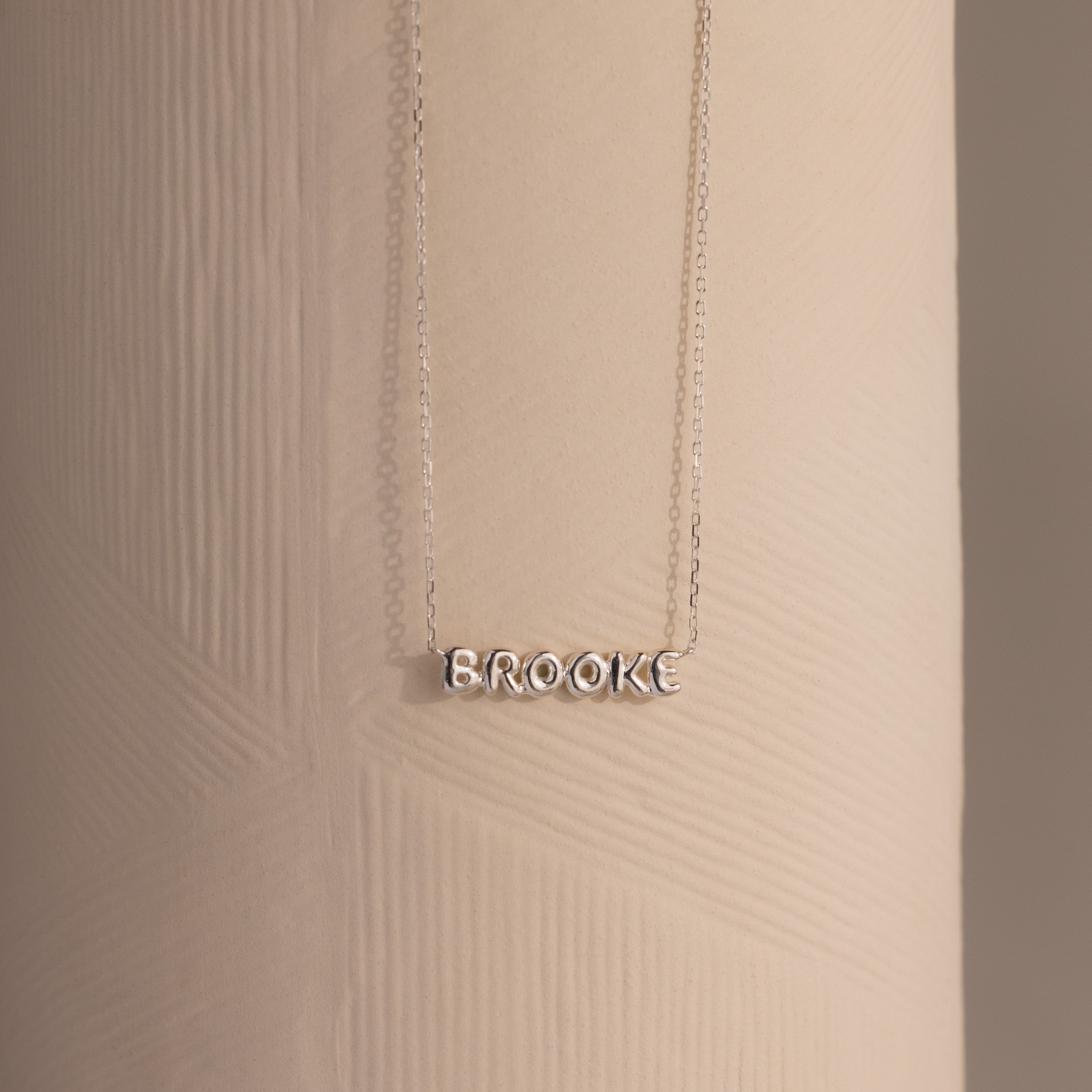 Dainty silver Brooke bubble name plate necklace displayed against a neutral surface.