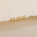A row of pairs of small gold hoop earrings, each adorned with a square-cut gemstone in 3 colors: light purple, blush pink, and aqua blue, displayed against a textured off-white background.
