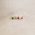 Four Raindrop Peridot Studs with gold settings and green gemstones are arranged in a row on beige fabric.